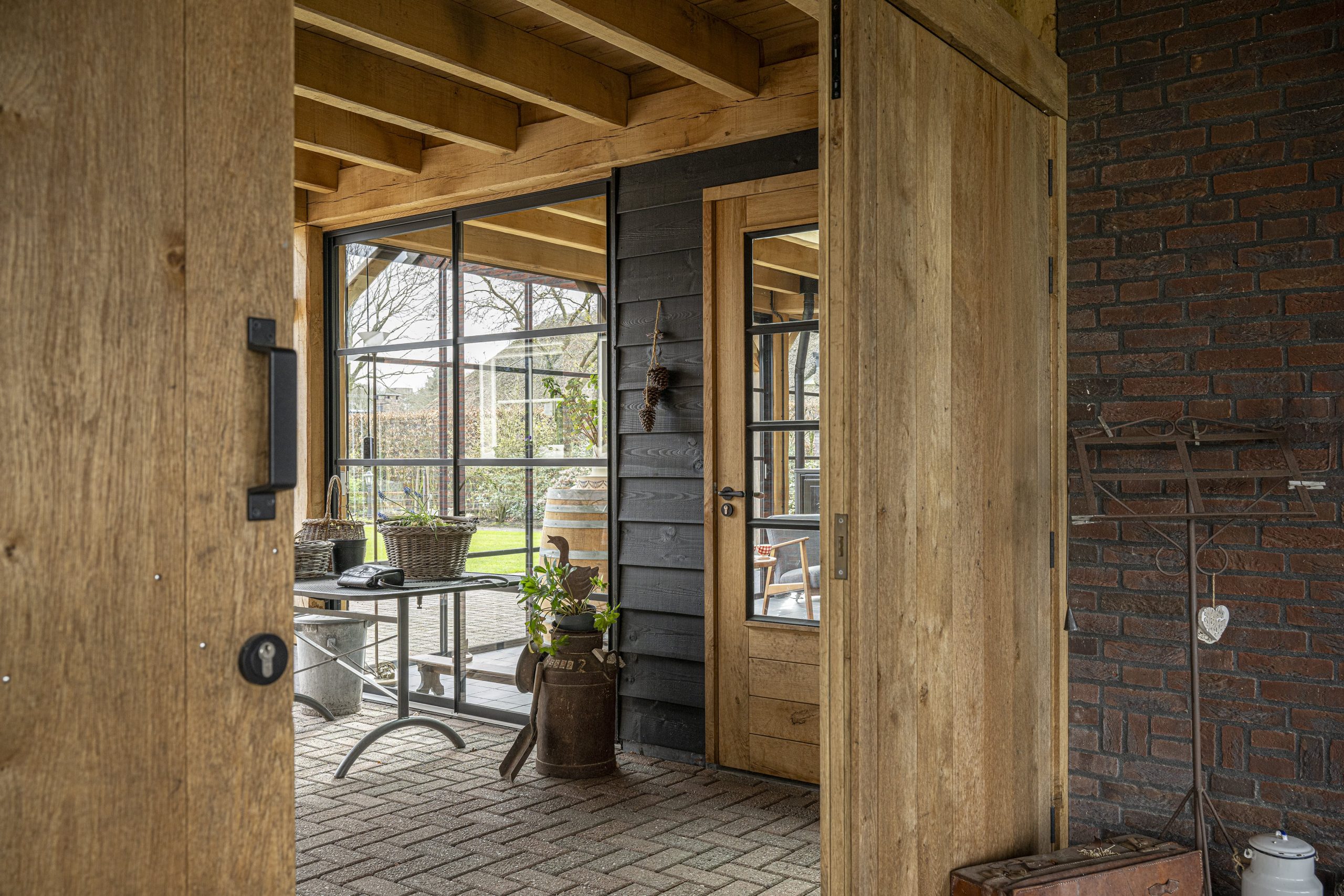 Doorkijk door de wijd openstaande eikenhouten schuifdeuren naar het ingerichte terras van de overkapping met zwarte wanden.