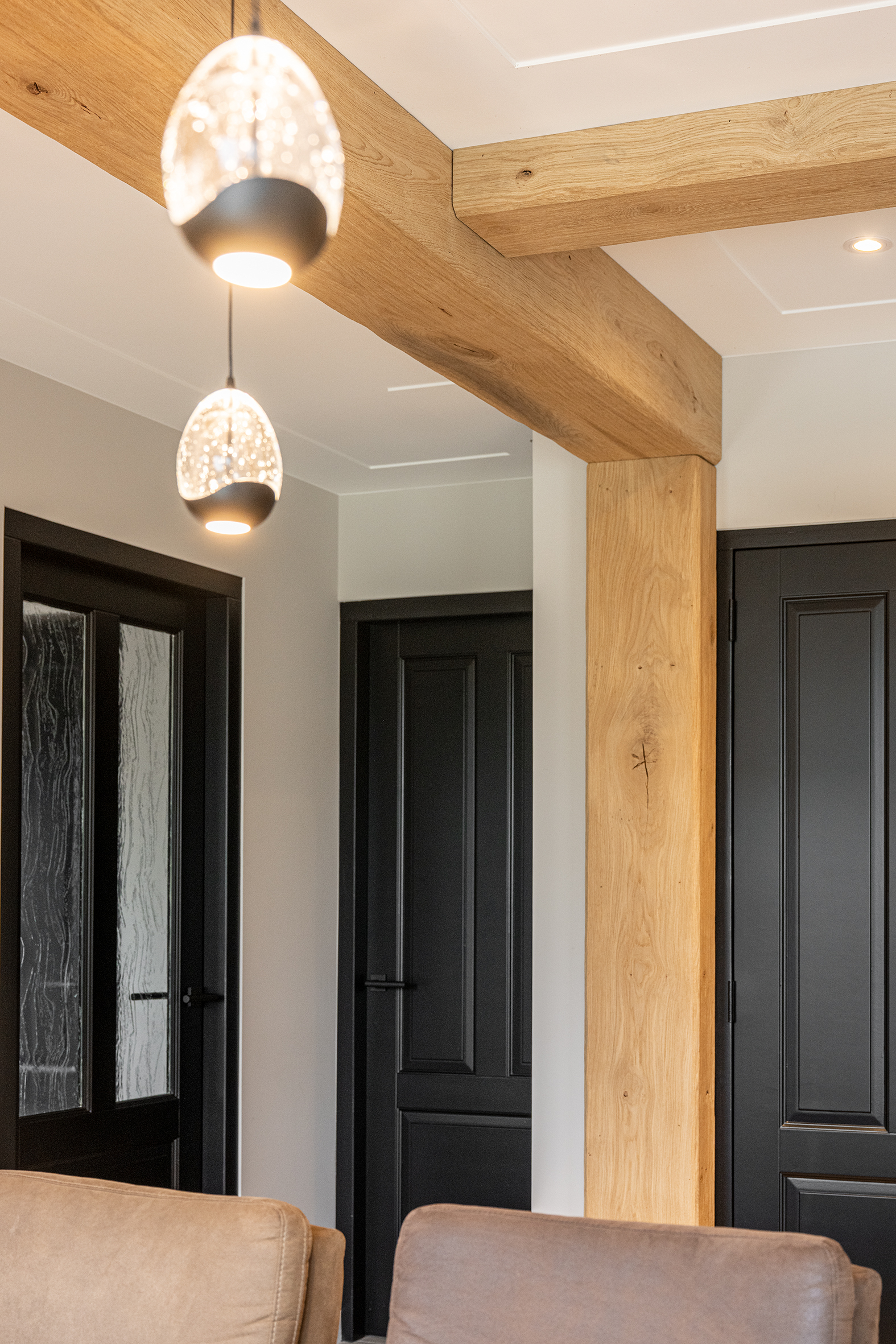 Close-up van twee zwarte paneeldeuren en een eikenhouten balkconstructie met sfeervolle hanglampen op de voorgrond.