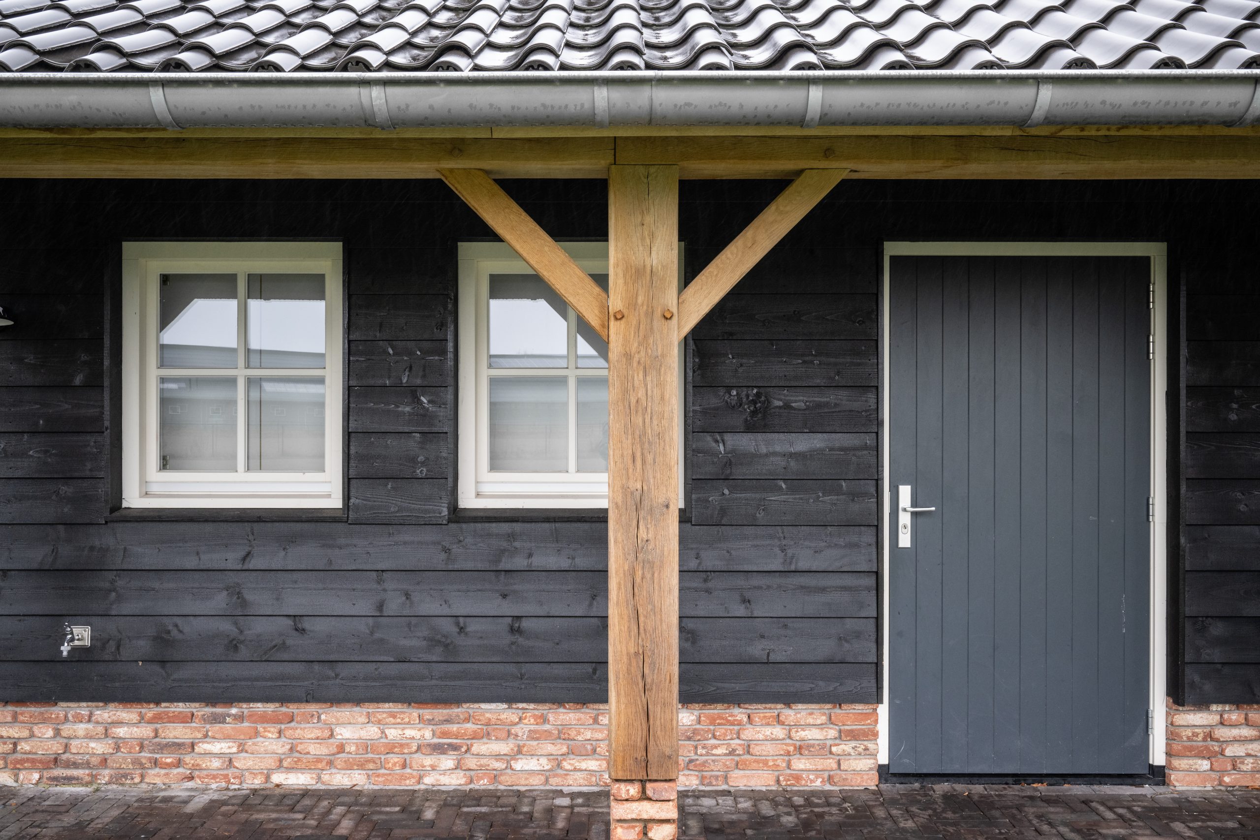 Gevelaanzicht van zwarte houten rabatdelen gecombineerd met een eikenhouten steunpilaar op een gemetselde voet.