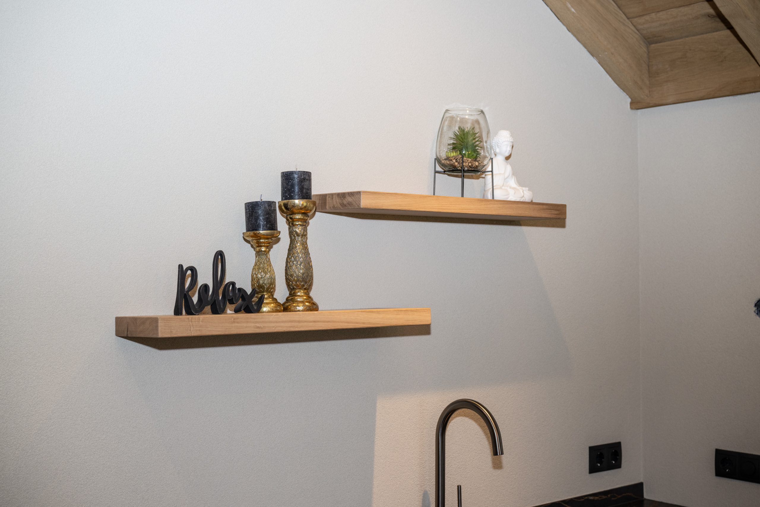 Detail van massief eikenhouten zwevende wandplanken met sfeervolle decoratie tegen een strak gestuukte wand.