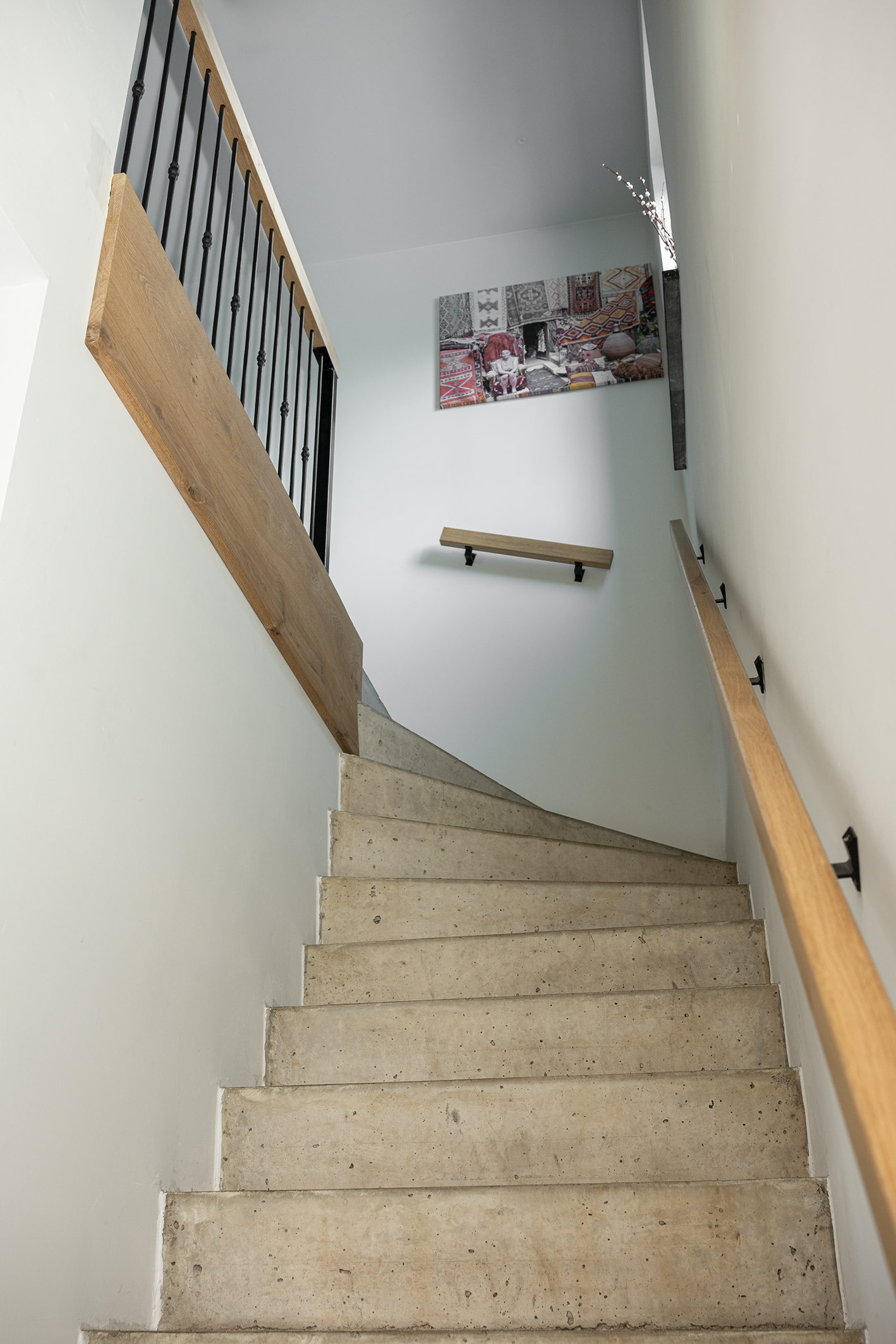 Een strakke, minimalistische trap van gegoten beton die omhoog loopt in een lichte hal met eikenhouten trapleuning