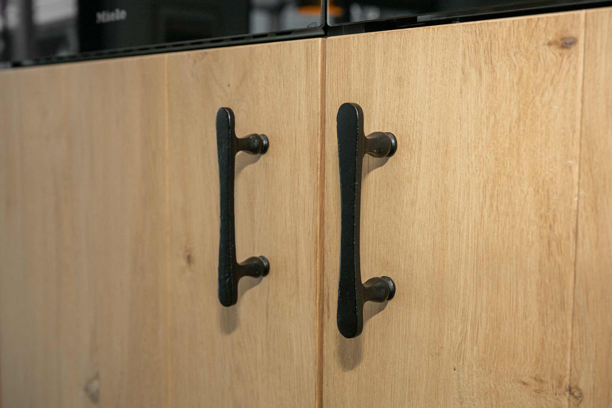 Close-up van zwarte, handgesmede deurgrepen op verticale eikenhouten keukenkastjes.