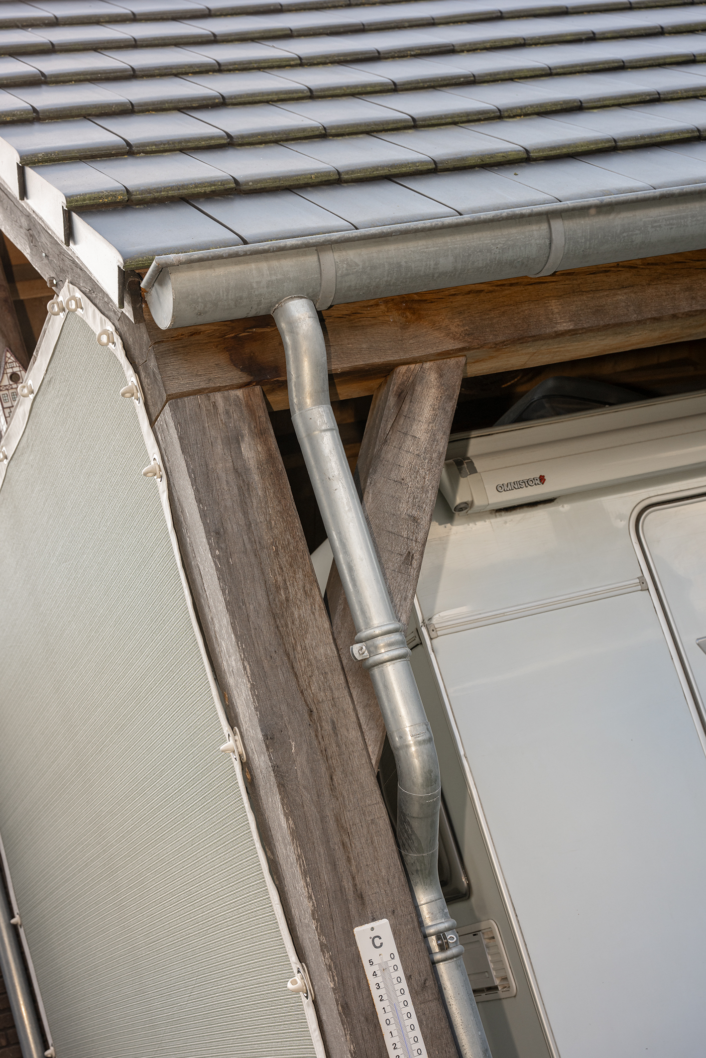 Detailopname van een zinken regenpijp en dakgoot gemonteerd op een zware eikenhouten balkenconstructie van een schuur of overkapping.