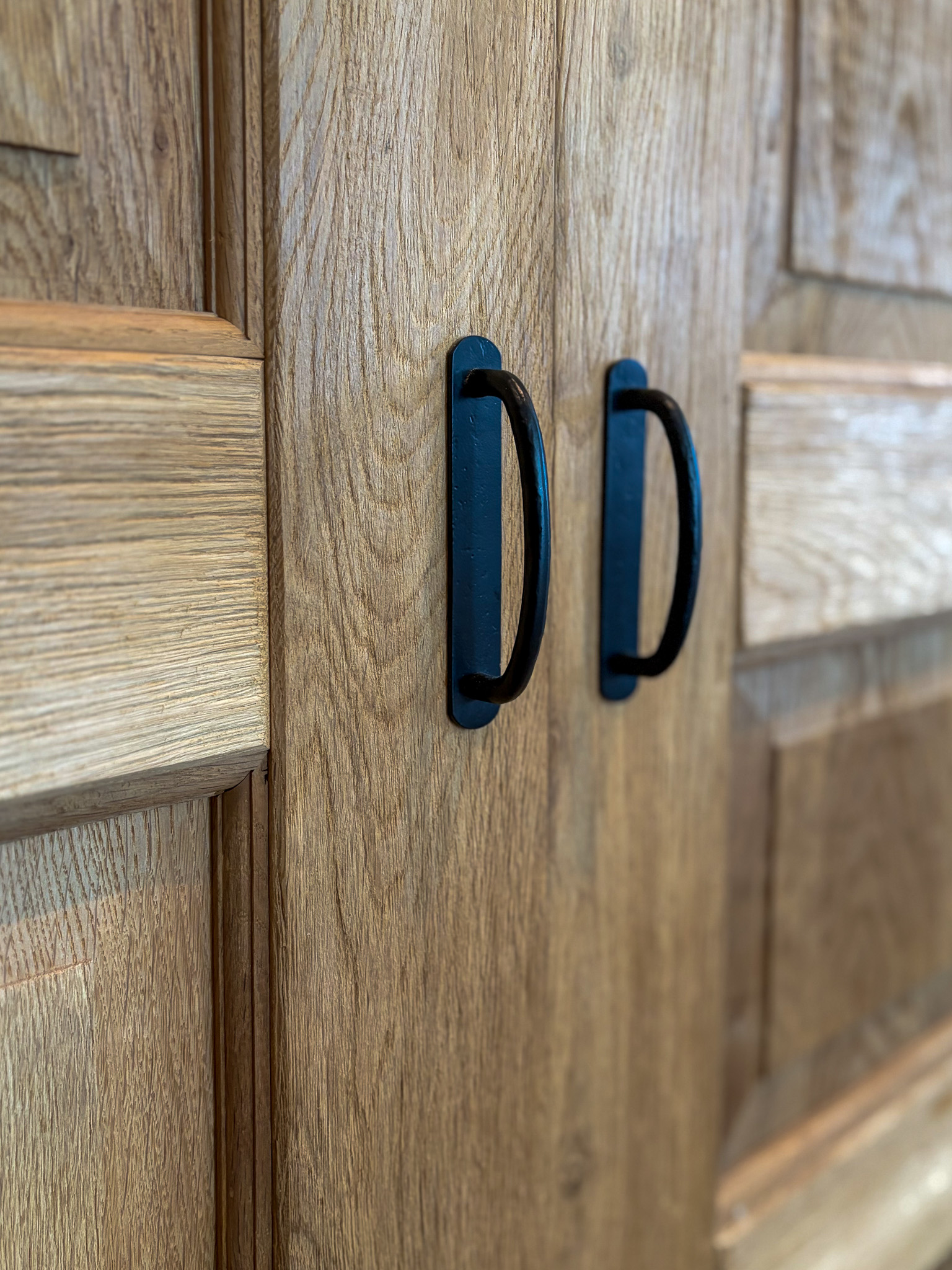 Close-up van twee zwarte, handgesmede metalen handgrepen op de eikenhouten deuren.