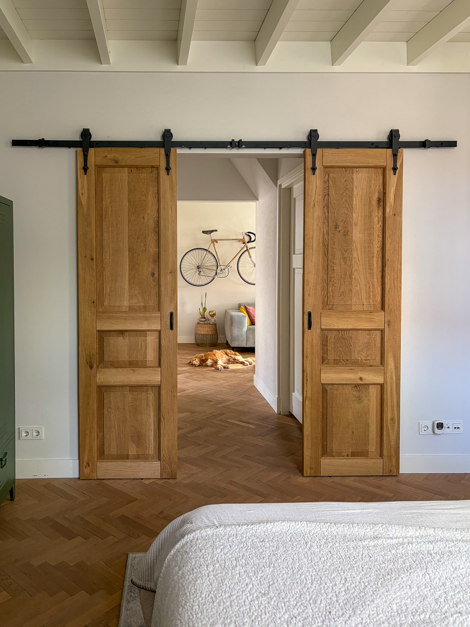 Perspectief vanuit een lichte hal met een witte deur, kijkend naar de gesloten eikenhouten schuifdeuren aan het einde van de gang.