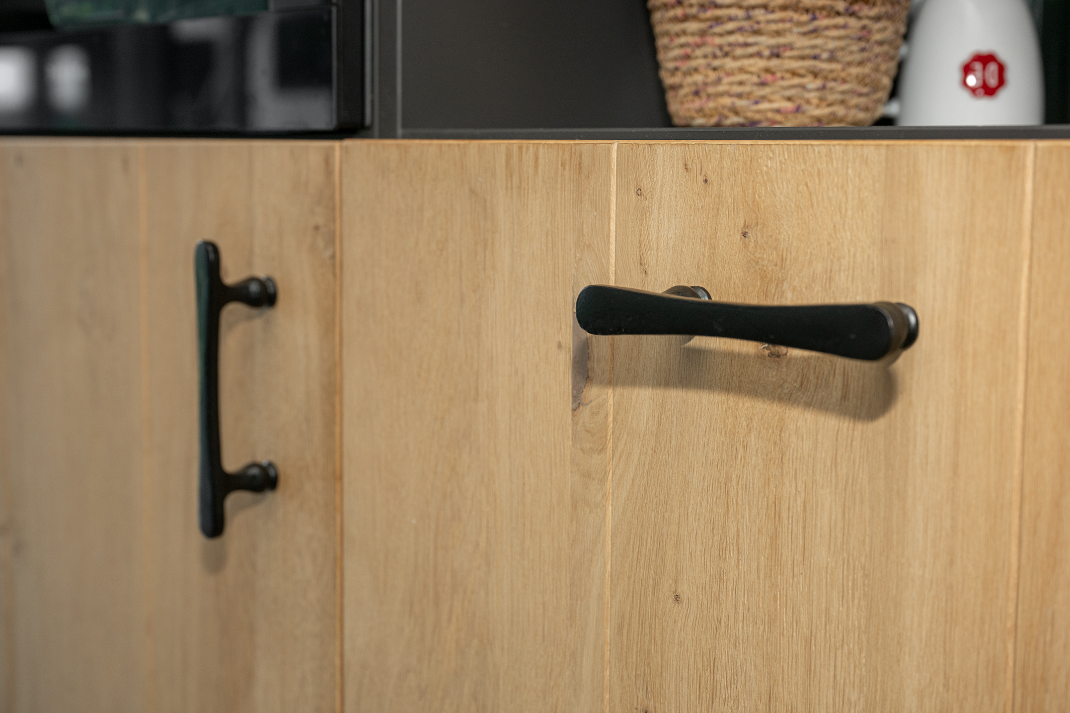 Detail van een eikenhouten kastdeur met een horizontale zwarte deurgreep in een modern landelijk interieur.