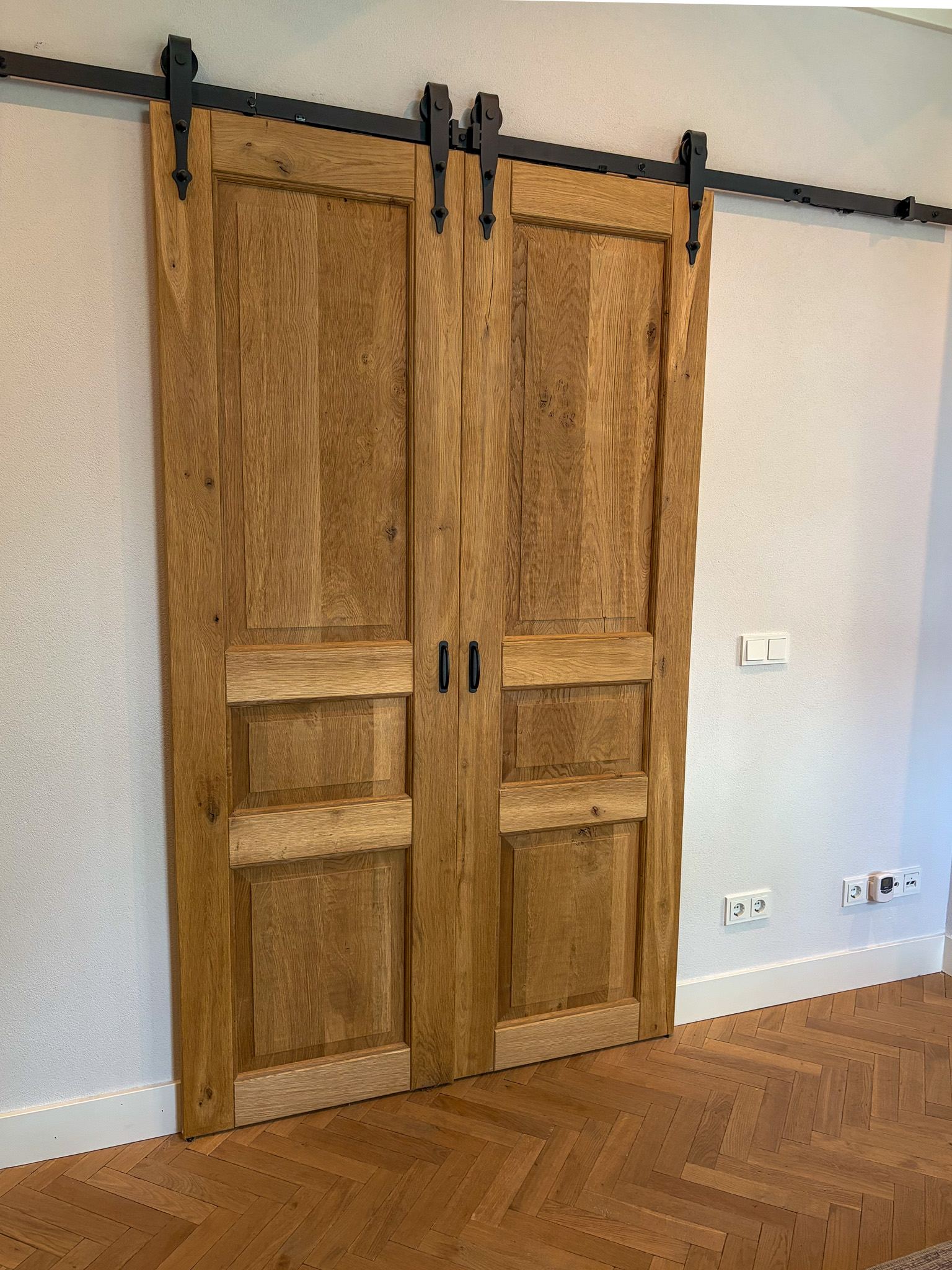 Dubbele eikenhouten paneeldeuren aan een zwarte rail, gezien vanuit een hoek in de slaapkamer.