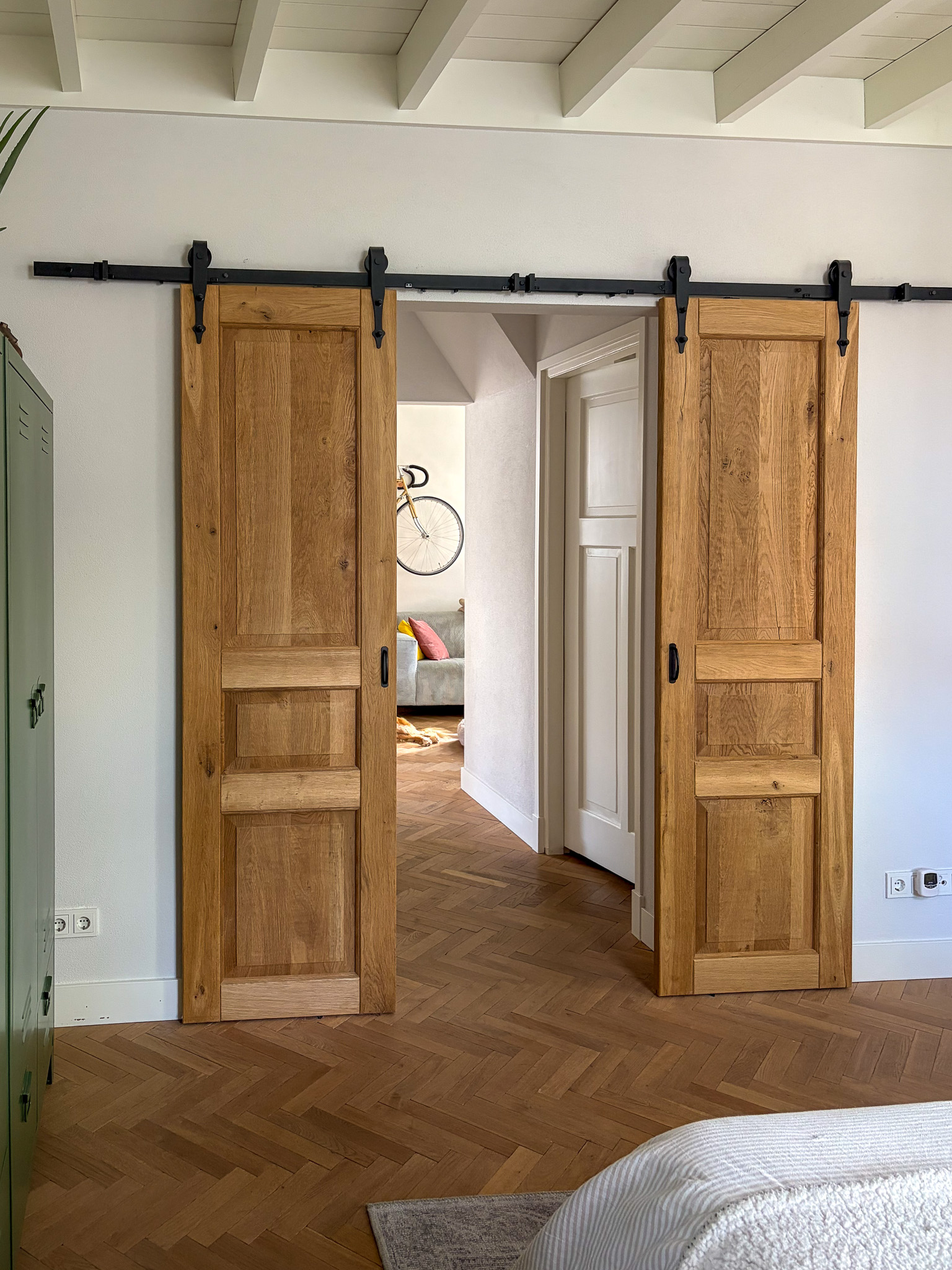 Gezicht vanuit de hal op de gesloten eikenhouten schuifdeuren, passend bij de warme houten visgraatvloer.