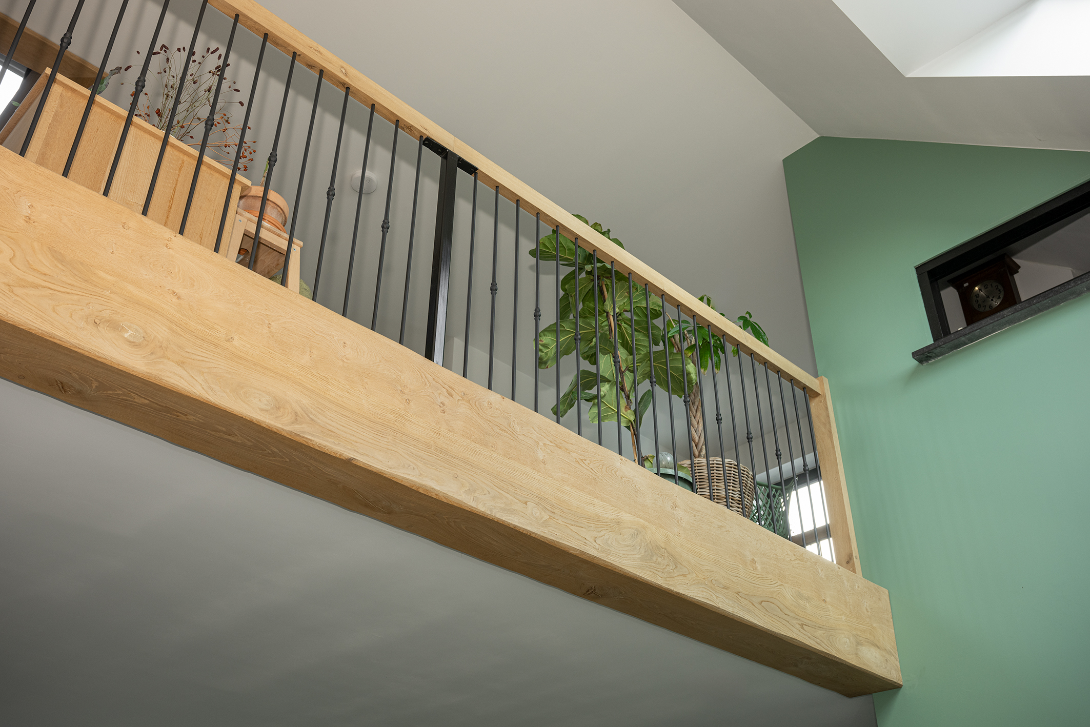 Detail van een vide met een eikenhouten balustrade en zwarte spijlen, versierd met kamerplanten.