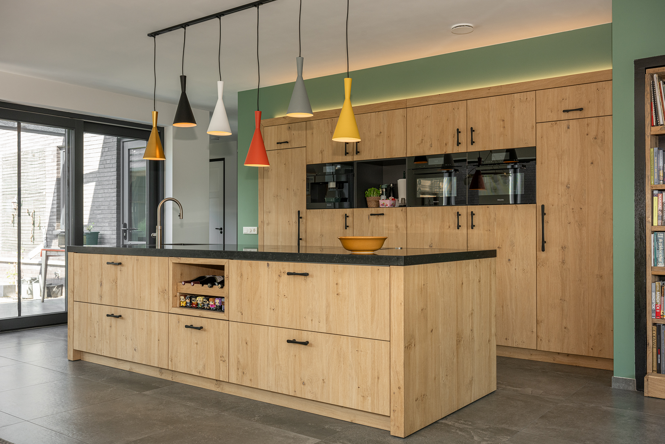 Detail van een houten kastenwand in de keuken met drie ingebouwde Miele ovens en een groene accentmuur.