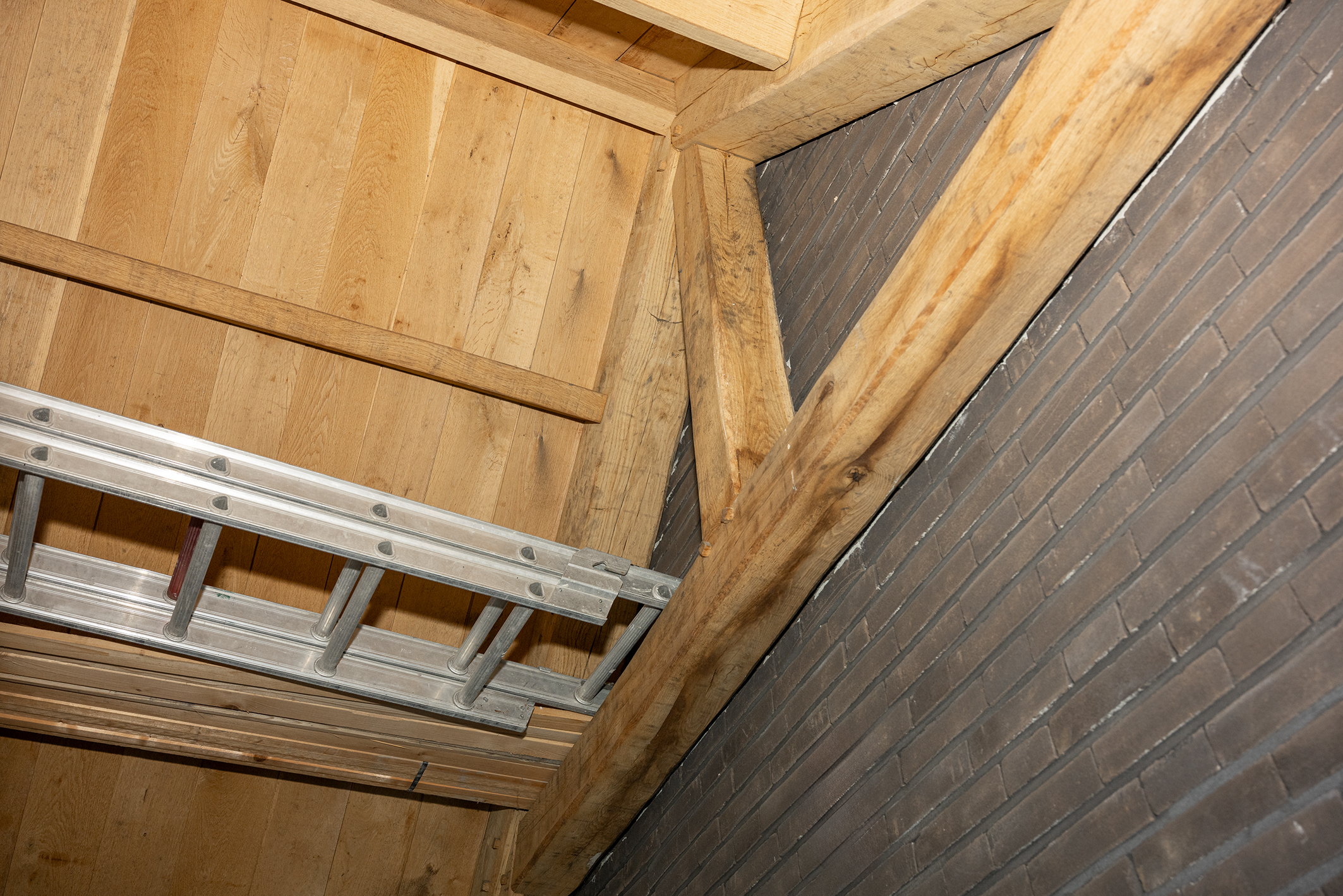 Blik op het plafond van een houten bijgebouw met een bakstenen muur en een vakwerkspant