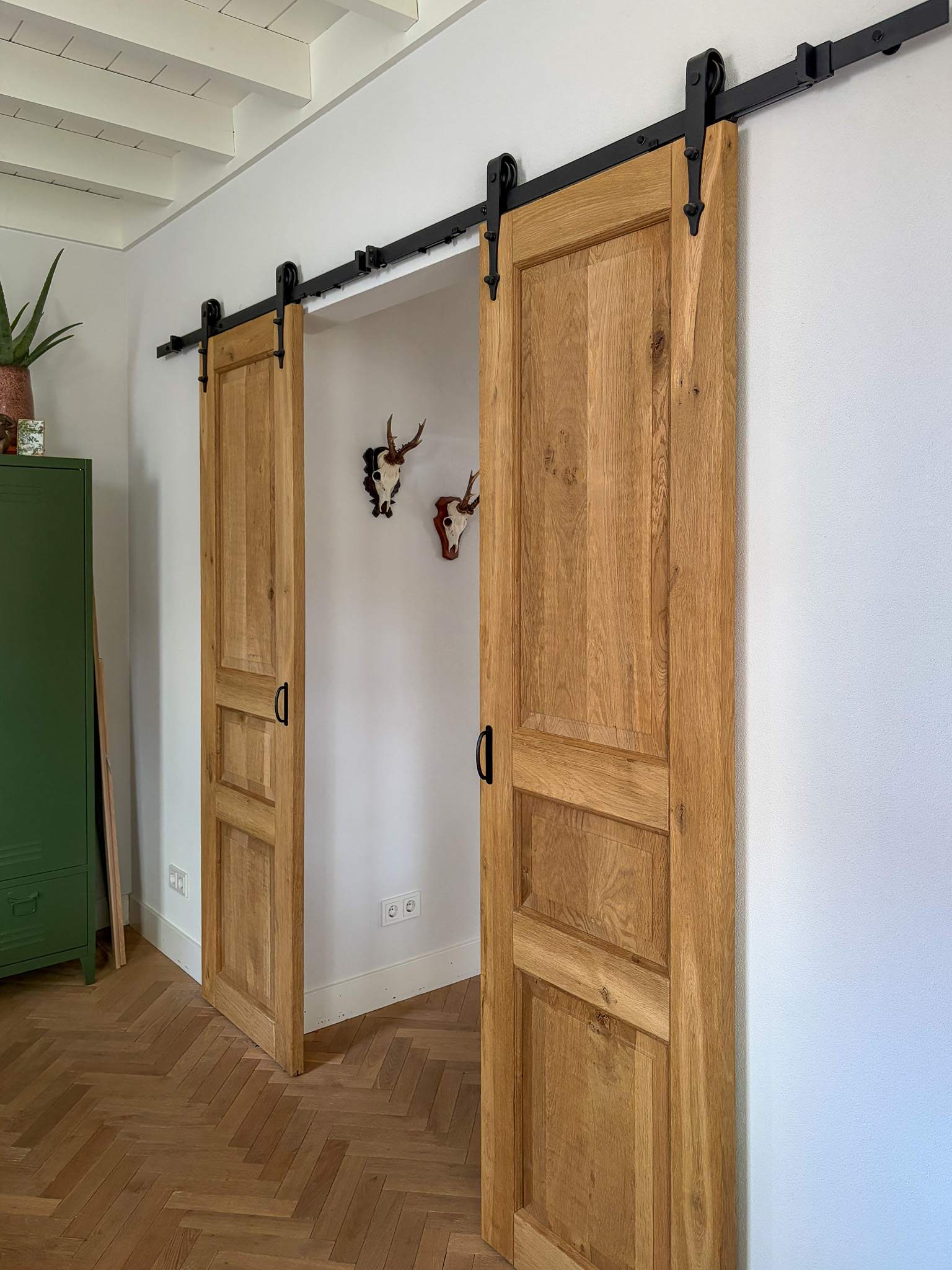 Slaapkamerinterieur met gesloten eikenhouten deuren, witte muren en een houten balkenplafond.