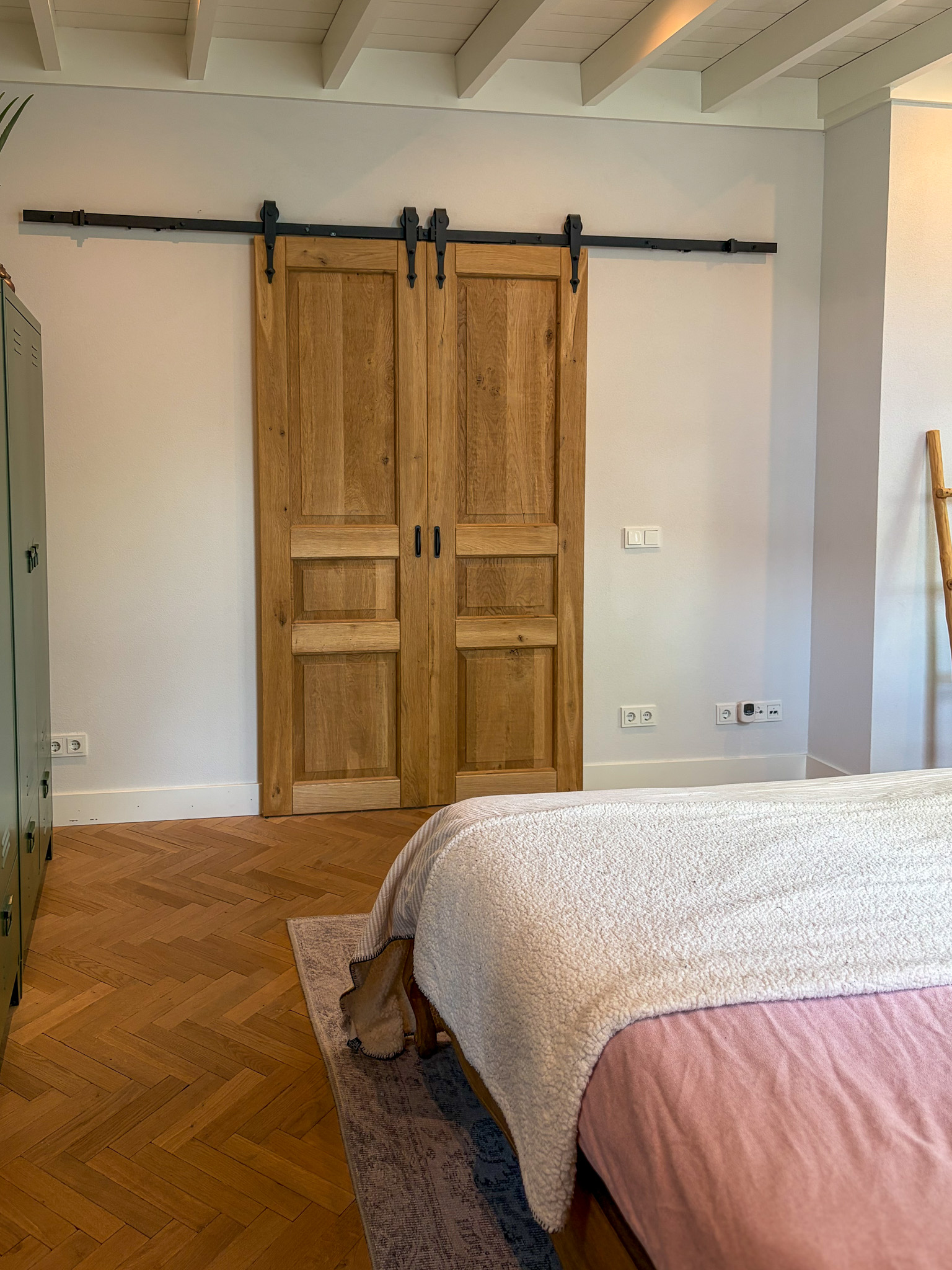 Vooraanzicht van twee gesloten massief eiken schuifdeuren met klassiek paneelontwerp en zwarte handgrepen tegen een witte wand.