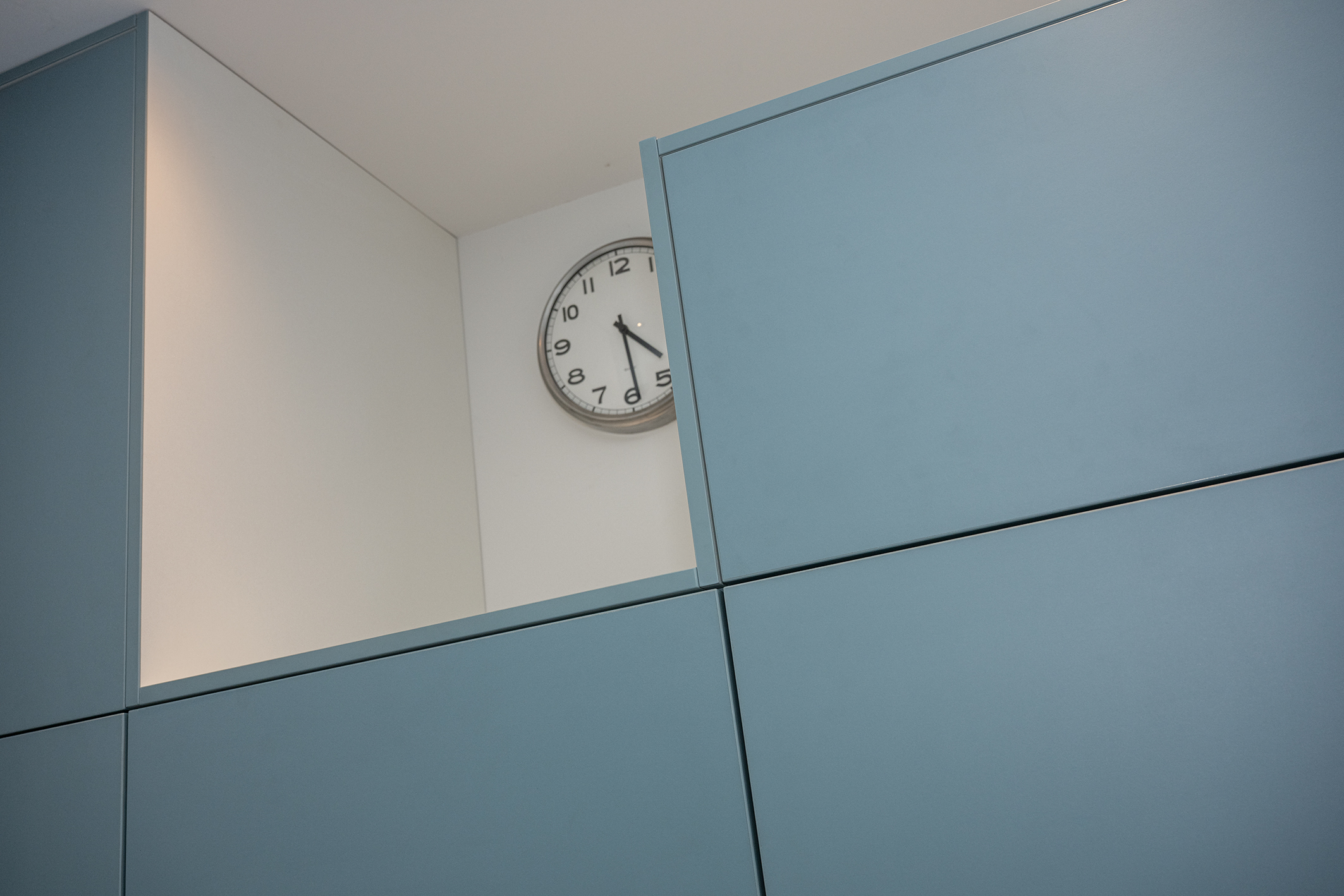Een open nis in een lichtblauwe kastenwand waarin een klassieke ronde stationsklok hangt.