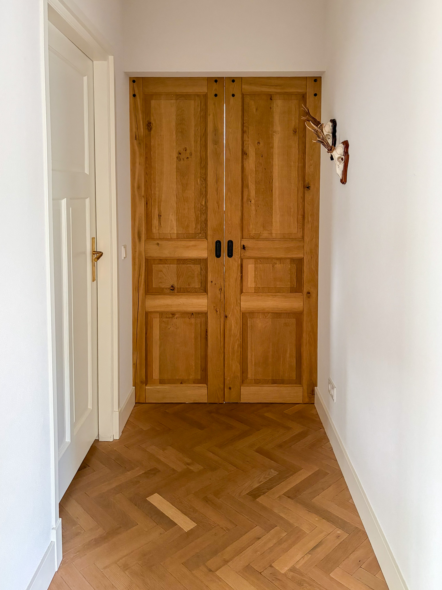 Detailopname van de onderkant van een eikenhouten deur die vlak boven een lichte eiken visgraatvloer hangt.