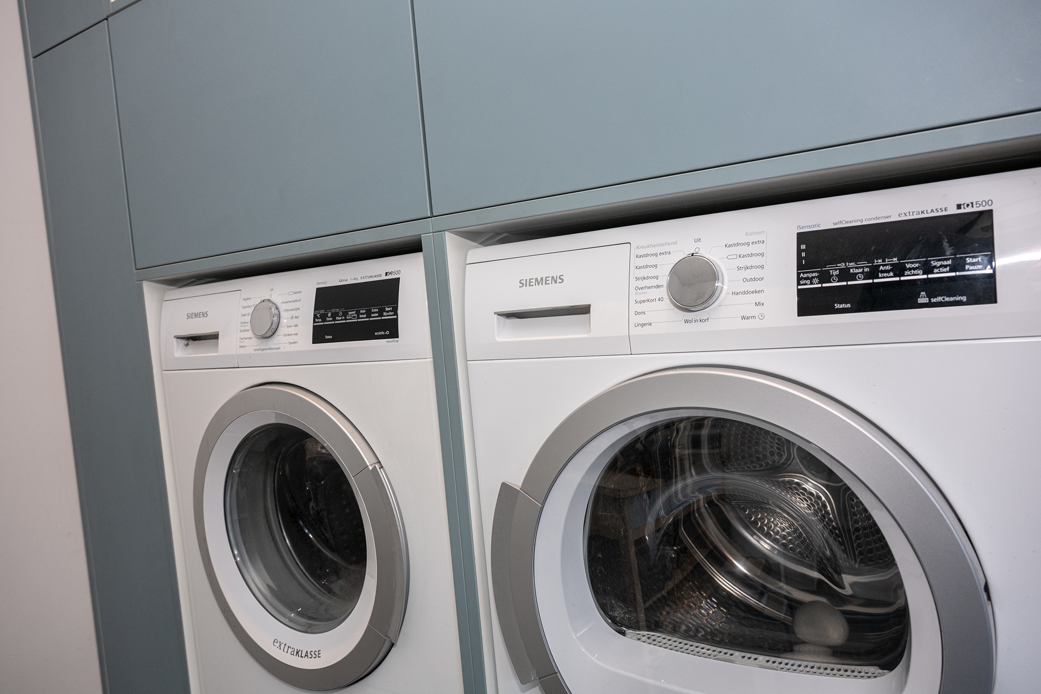 Siemens wasmachine en droger strak ingebouwd in een lichtblauwe op maat gemaakte kastenwand.