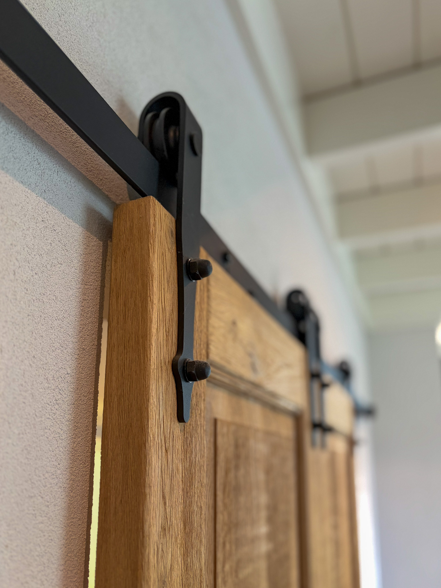 Zij-aanzicht van het zwarte schuifdeurbeslag (wiel en rail) gemonteerd op een dikke eikenhouten deur.