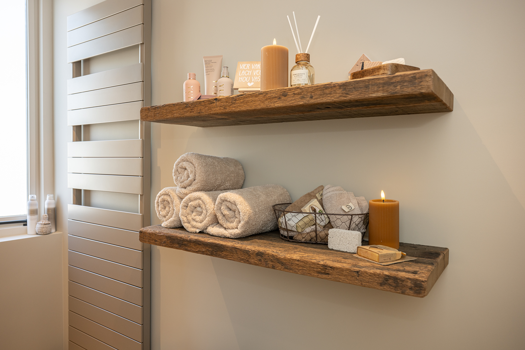 Een foto van twee houten wandschappen, met focus op de decoraties, waaronder handdoeken, kaarsen en verzorgingsartikelen.