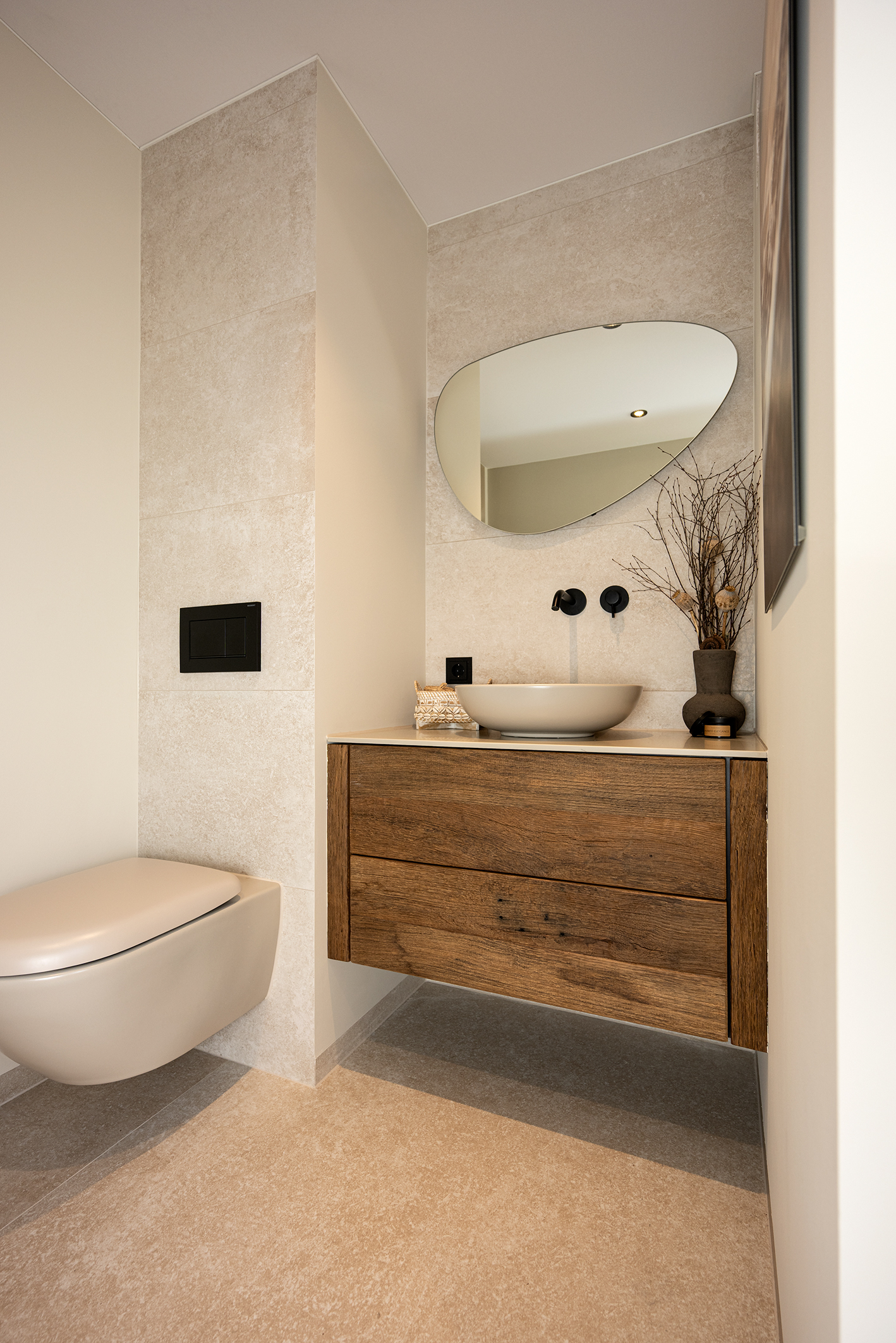 Een grotere overzichtsfoto van een badkamerhoek met een zwevend eikenhouten wastafelmeubel, een bijpassend toilet en de verlichte spiegel, allemaal in een rustieke stijl.