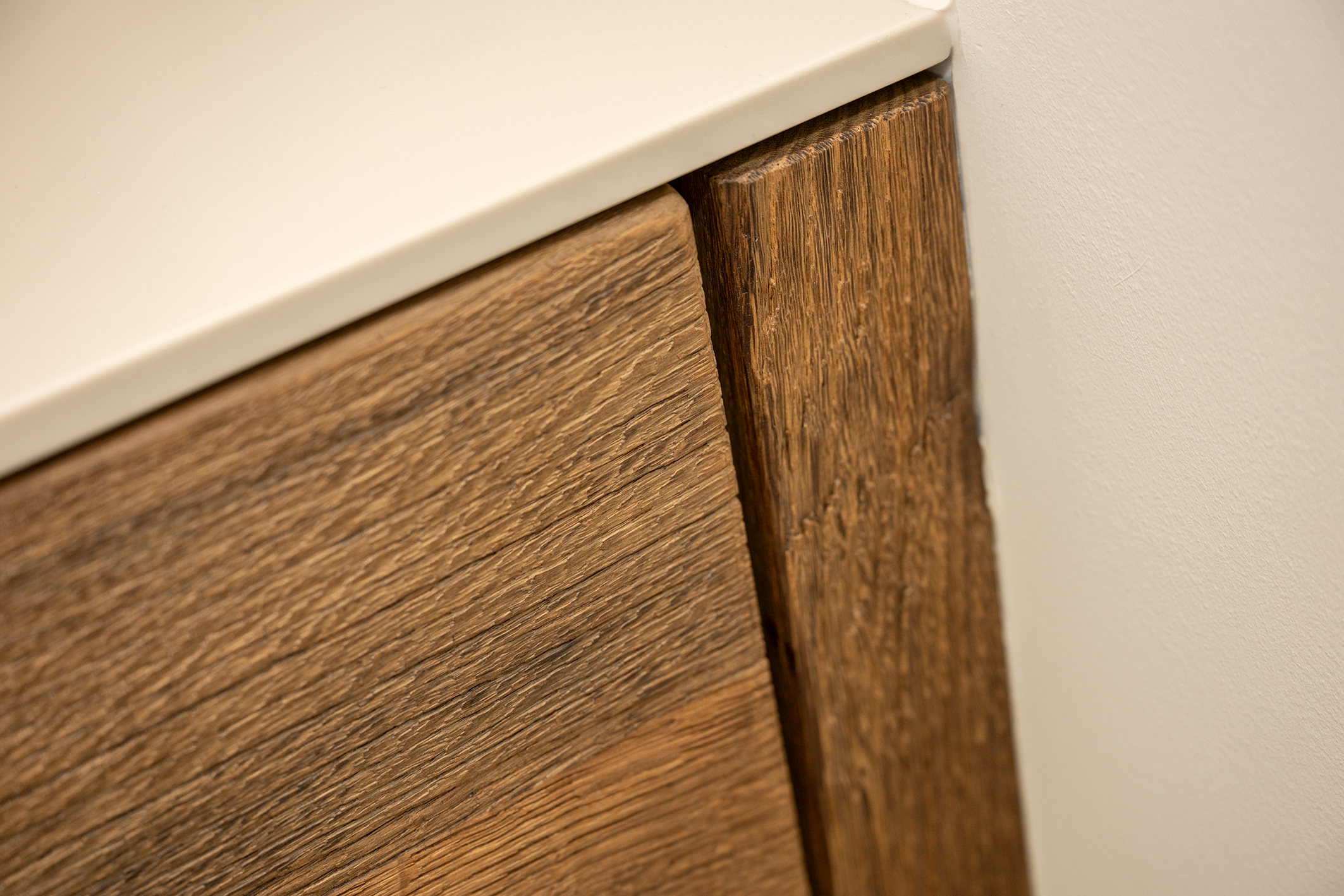 Een close-up van de hoek van het eikenhouten badkamermeubel en het witte wastafelblad, de textuur van het hout is goed zichtbaar.