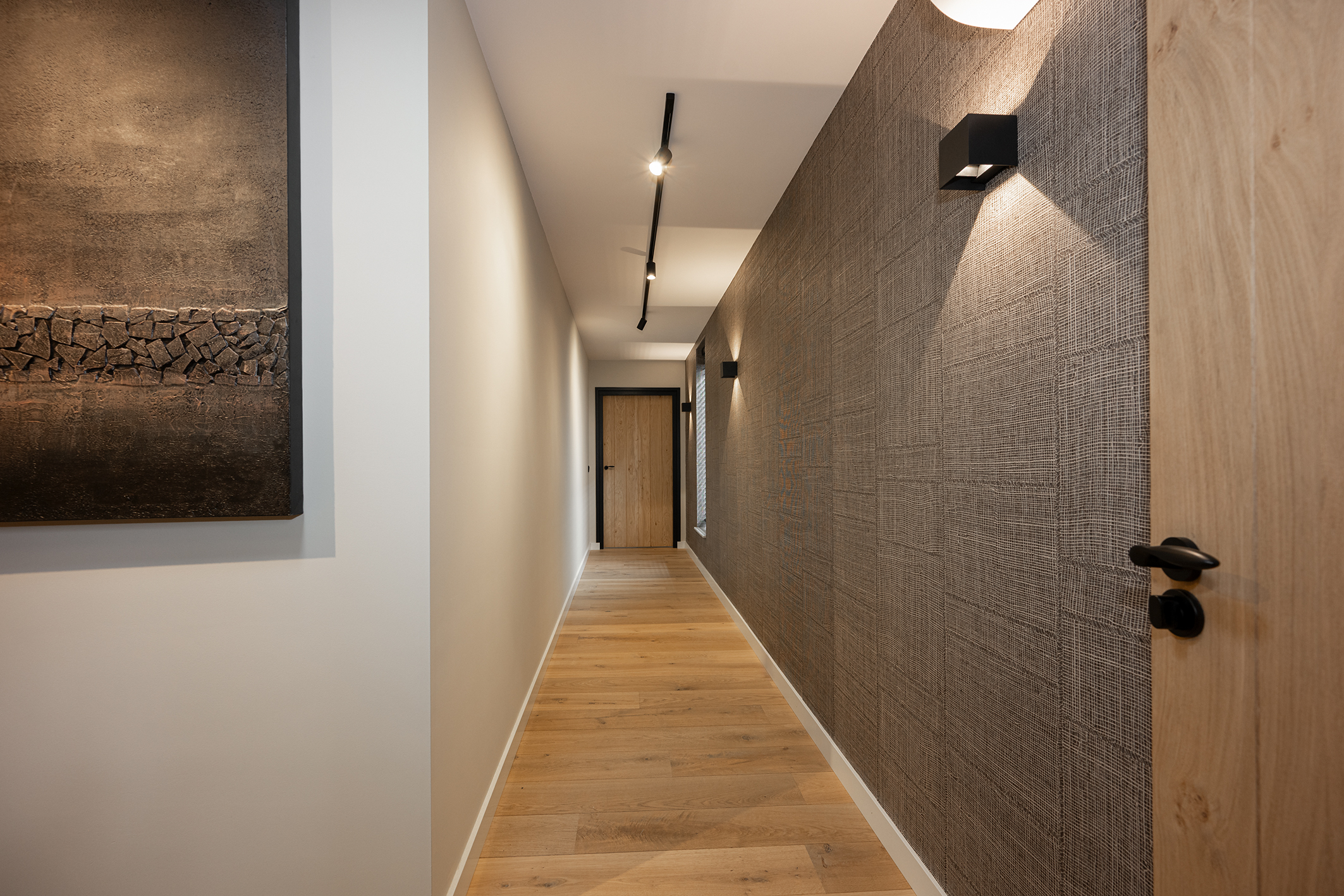 Een gang met houten deuren met zwarte kozijnen en handgrepen. Het getextureerde wandbehang is donkergrijs. Een airconditioner is aan de muur gemonteerd en er zijn wandlampen te zien. De vloer is van hout.