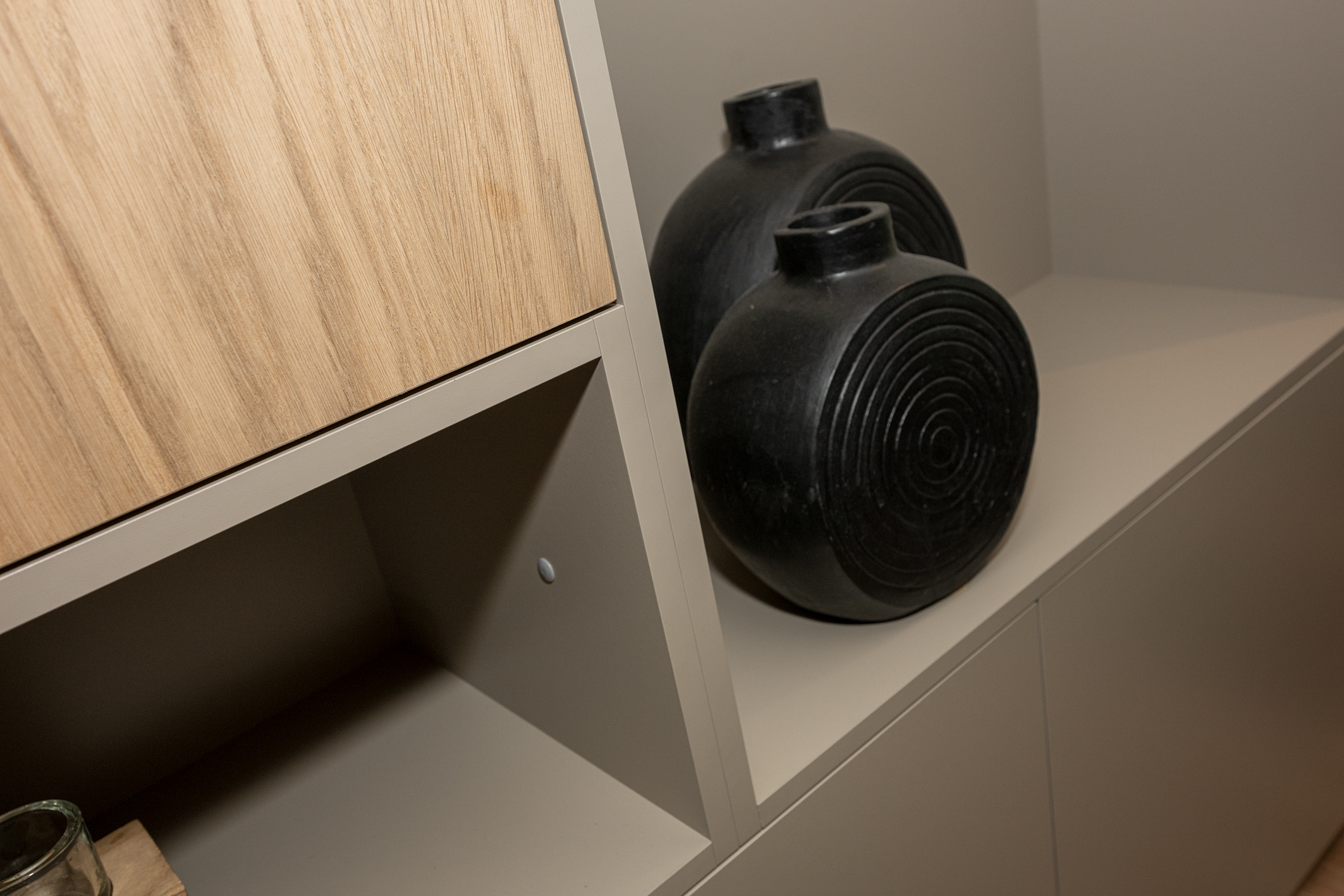 Twee zwarte, ronde designvazen met cirkelvormig reliëf in een nis van een moderne grijs beige kast.