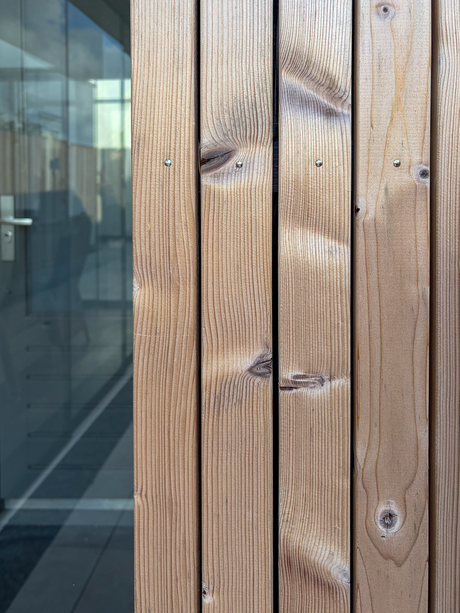 Een close-up van verticale houten gevelbekleding met duidelijke noesten en nerven, direct naast een glazen pui.