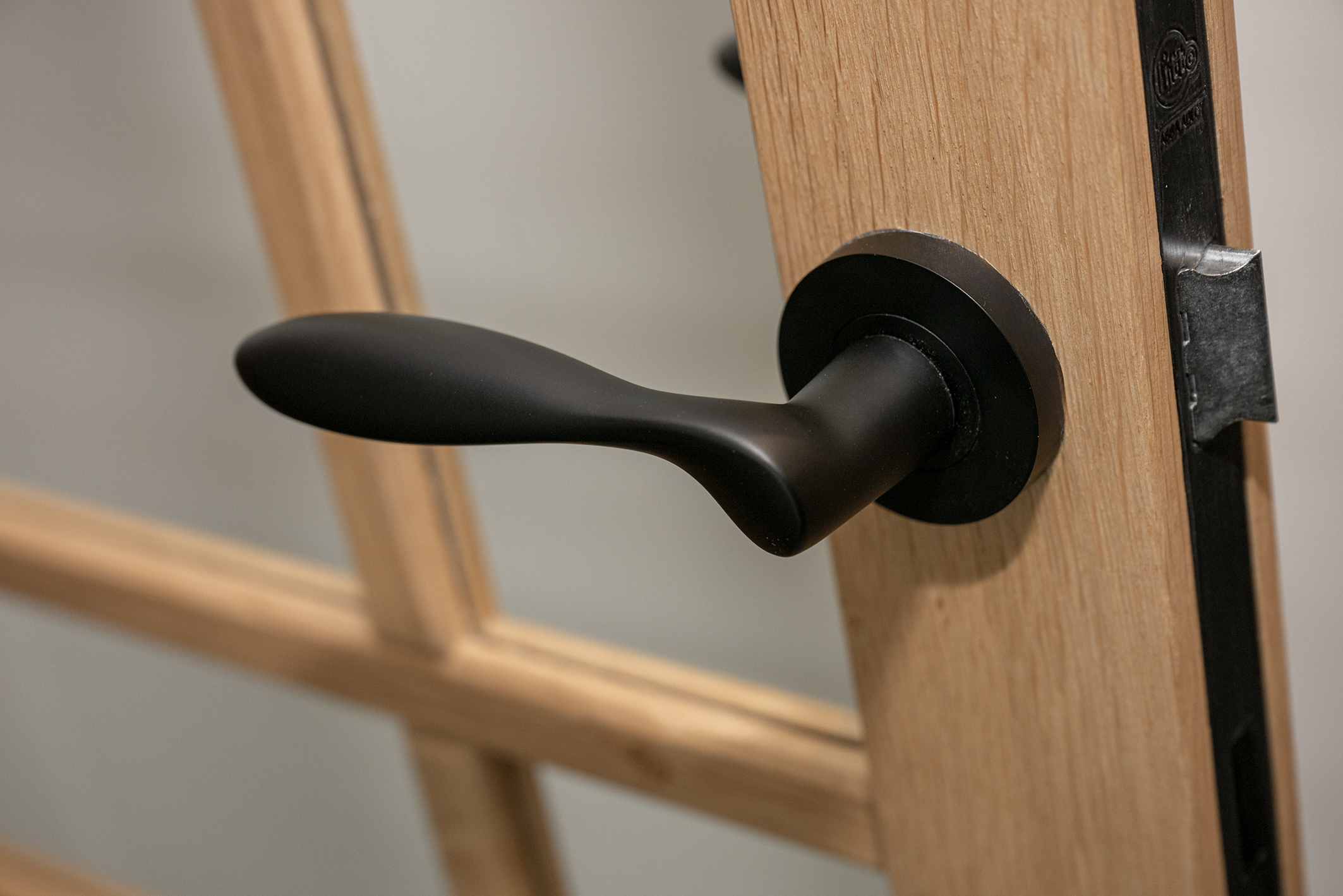 Close-up van een matzwarte deurkruk met een organisch design op een eikenhouten binnendeur met glas.