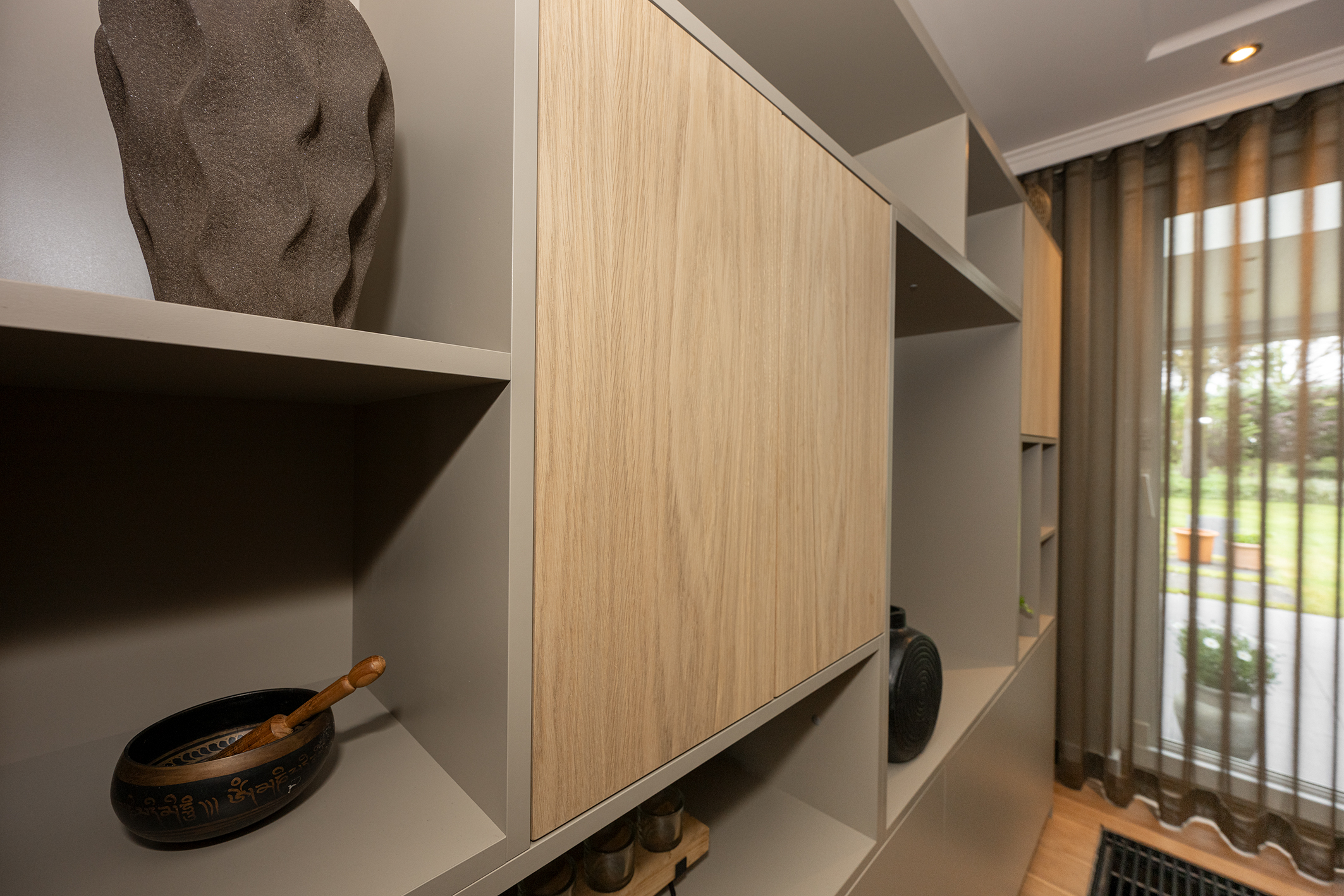 Close-up van een maatwerk vakkenkast in greige met eikenhouten deuren, gedecoreerd met een klankschaal en accessoires.