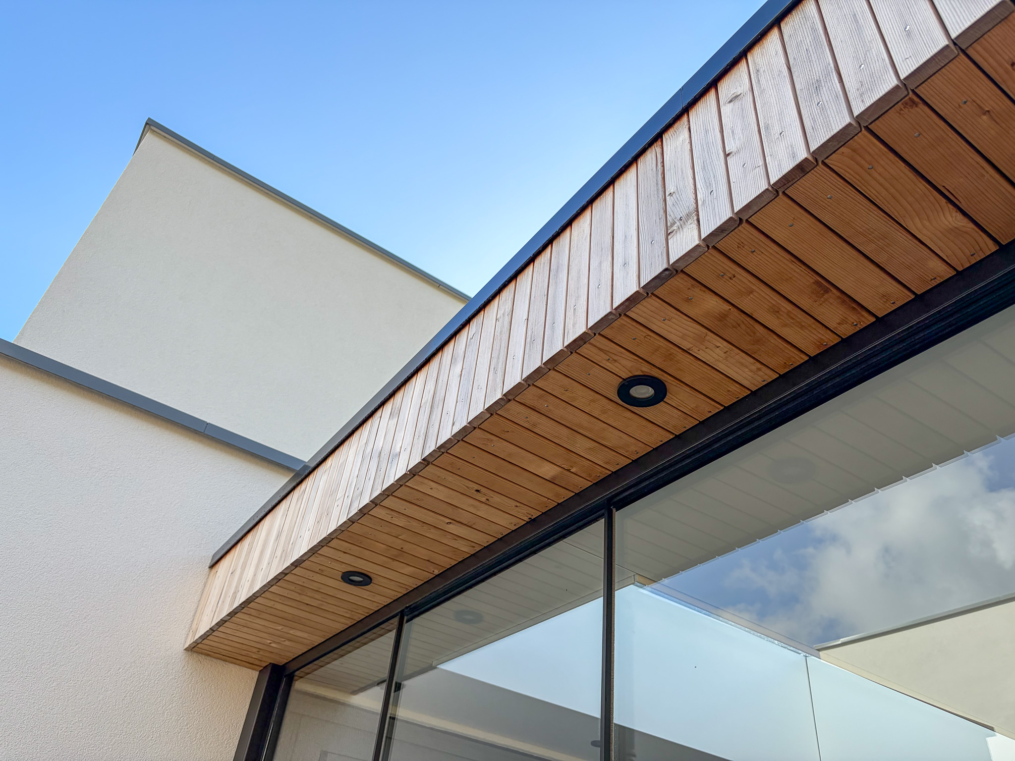 Gecombineerd aanzicht van een strak wit gestuukte muur met de houten afwerking van een moderne overkapping.