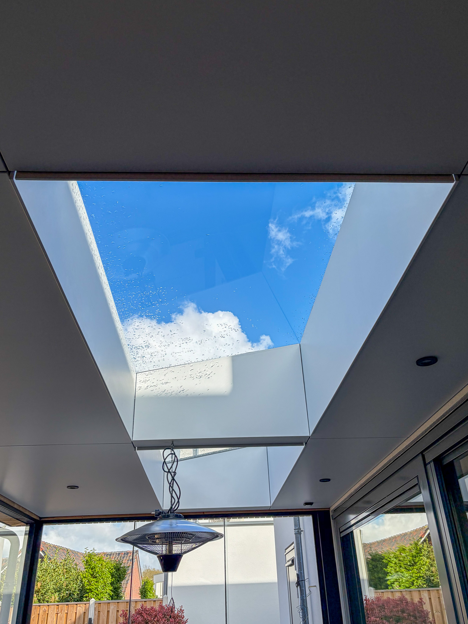 Een direct opwaarts aanzicht van de lichtstraat in het dak van de overkapping, die de blauwe hemel met witte wolken omlijst.
