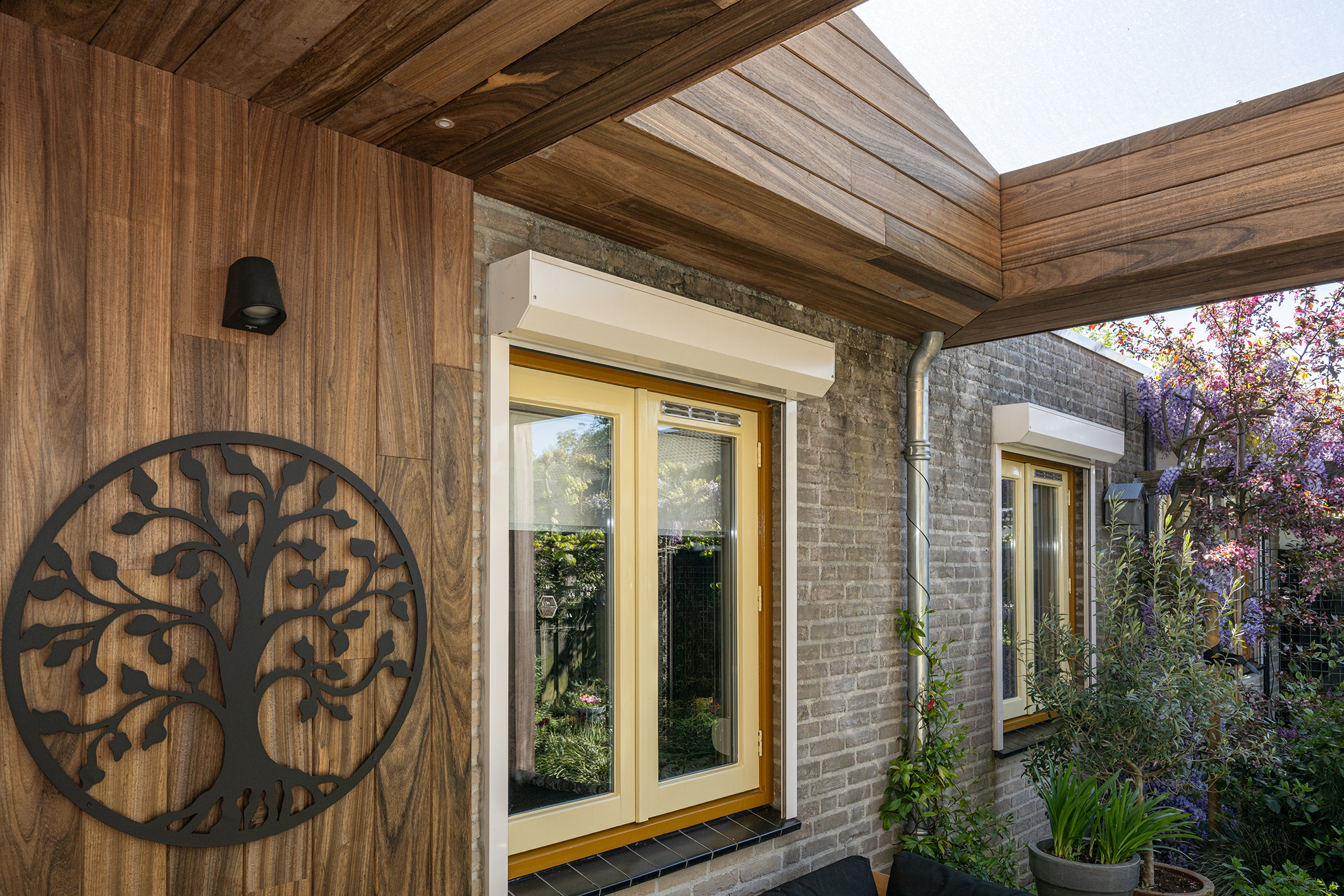 Luxe wandafwerking met padoek hout en een decoratieve zwarte levensboom naast een raamkozijn.