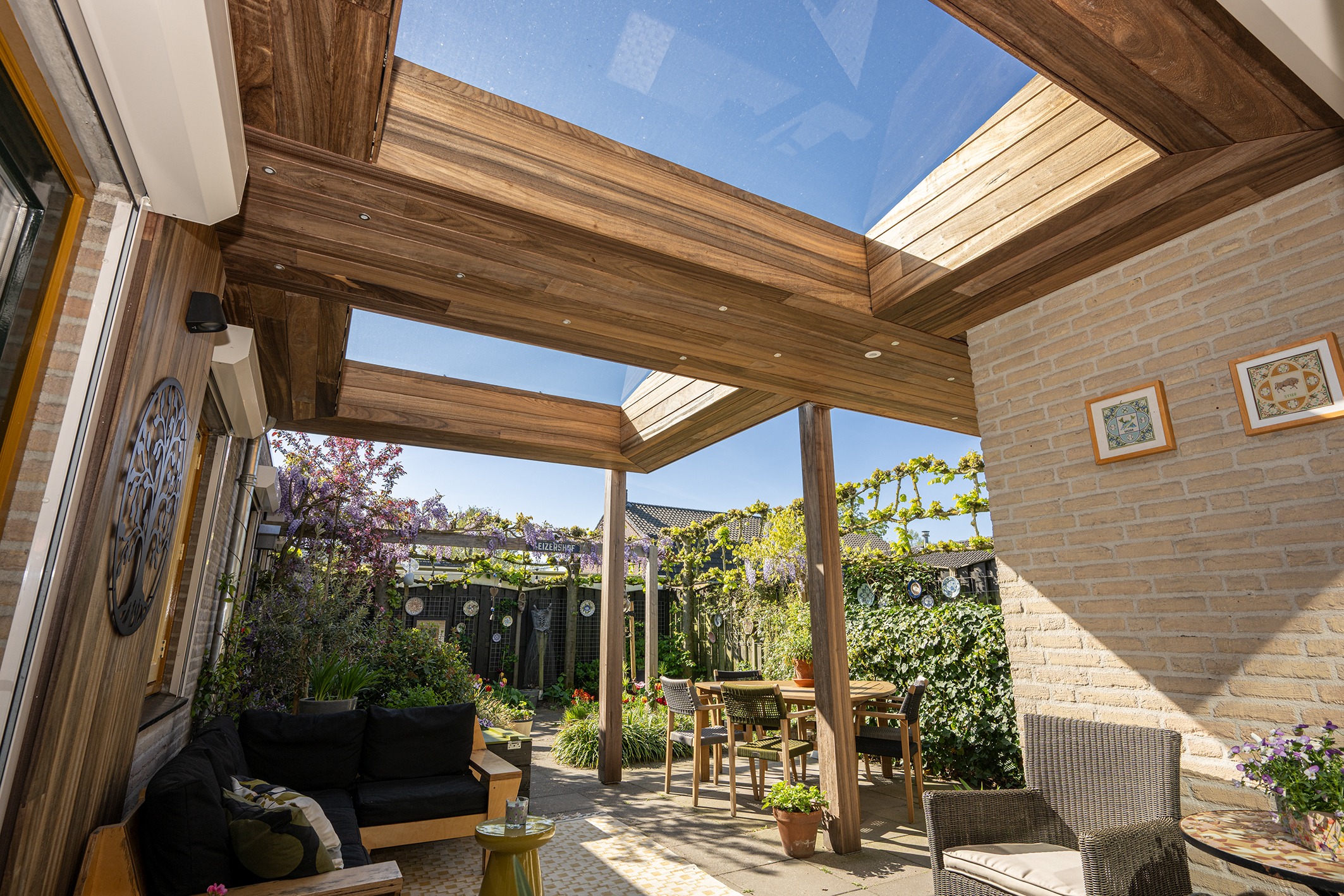 Moderne padoek overkapping aangebouwd aan een bakstenen woning met houten wandafwerking.