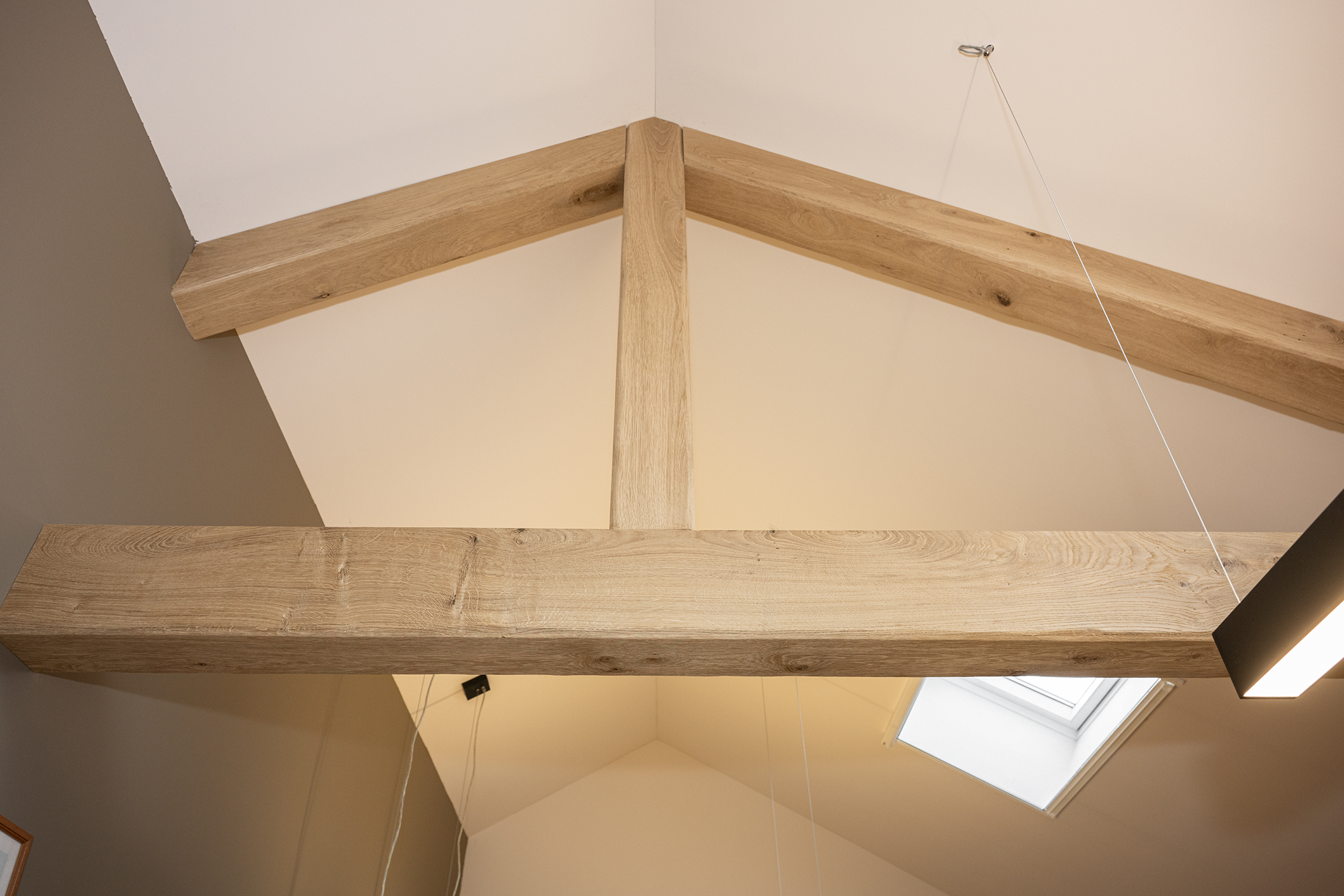 Zicht op de houten dakconstructie met robuuste eikenhouten balken tegen een hoog wit plafond.