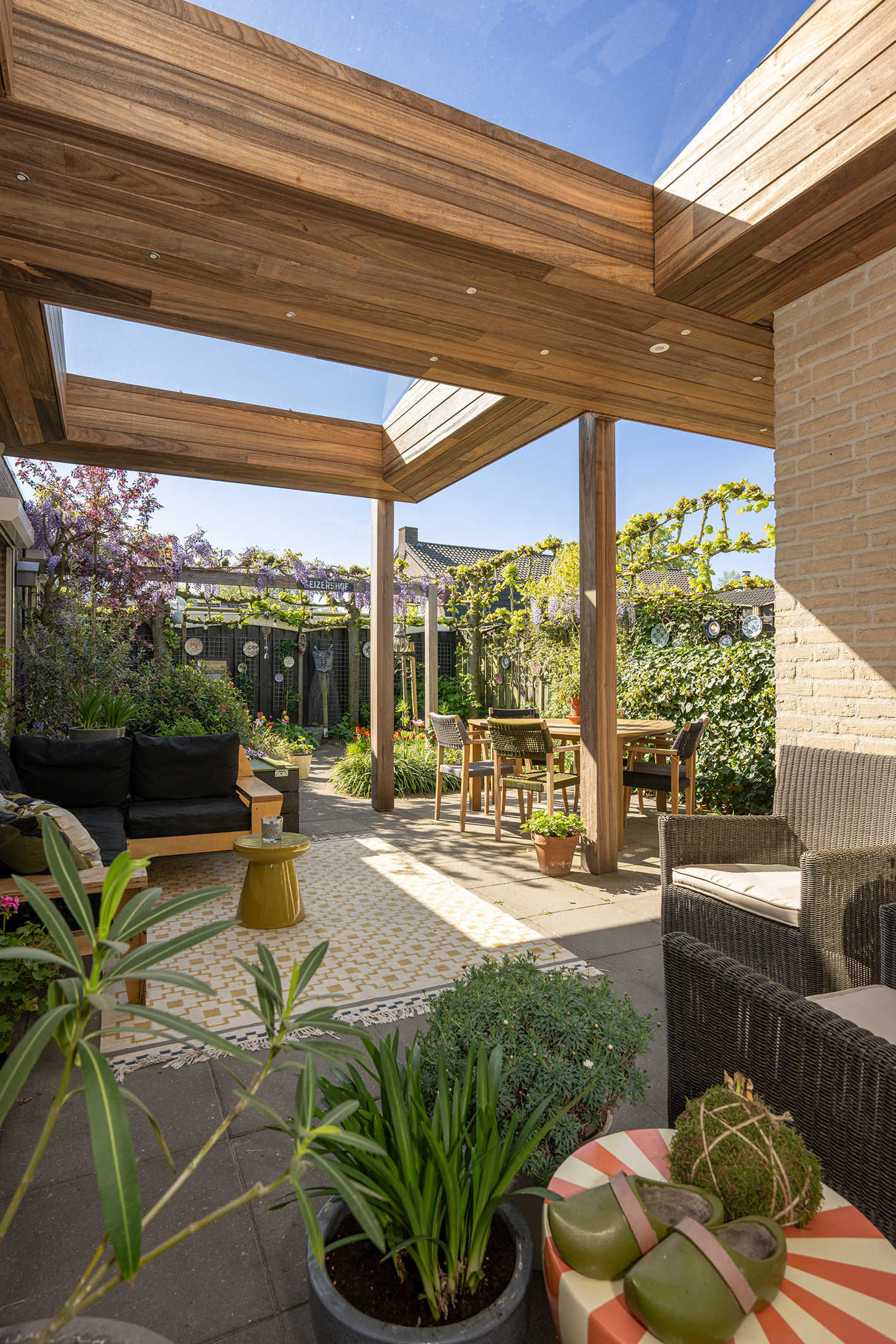 Sfeervol terras met loungebank onder een padoek houten overkapping met zicht op de tuin.