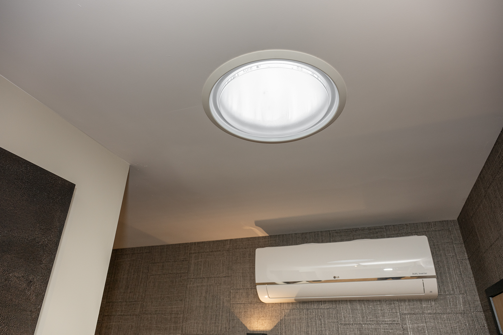 Ronde tube lichtkoepel in een strak wit plafond boven een LG wand-airconditioning unit.