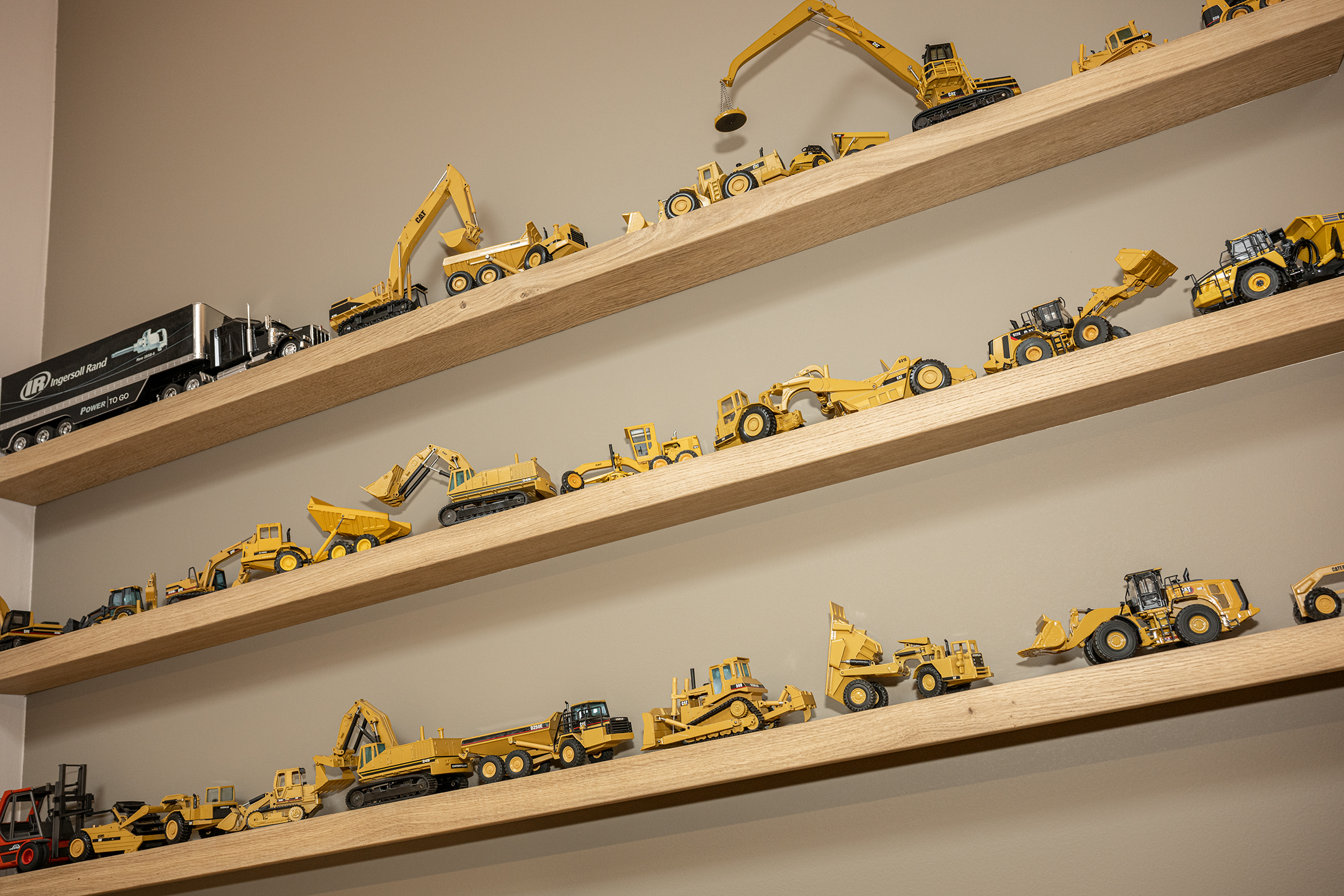 Vier houten wandplanken vol met een gedetailleerde verzameling van gele miniatuur graafmachines en bouwvoertuigen.