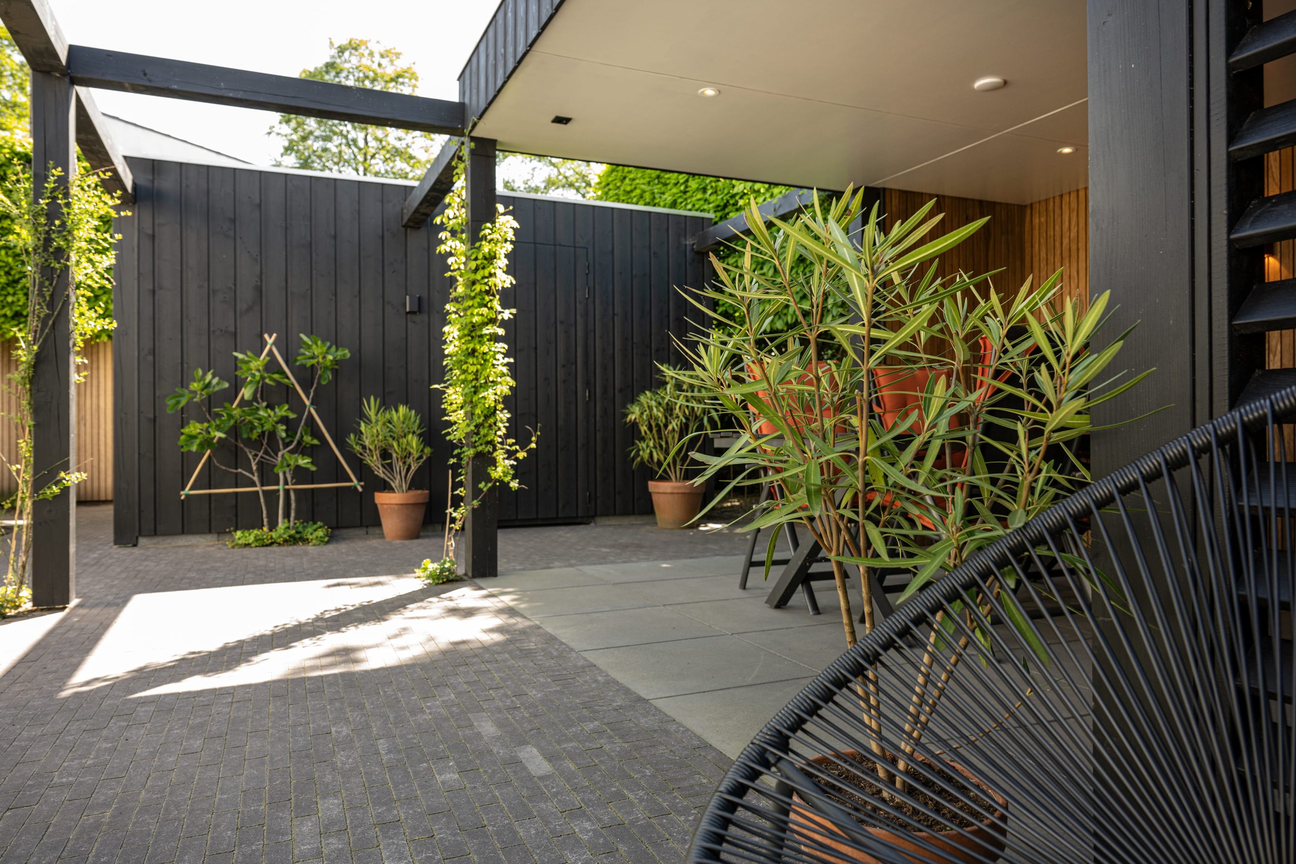 Modern terras met luxe overkapping van thermo fraké hout en zwarte thermo vuren accenten.