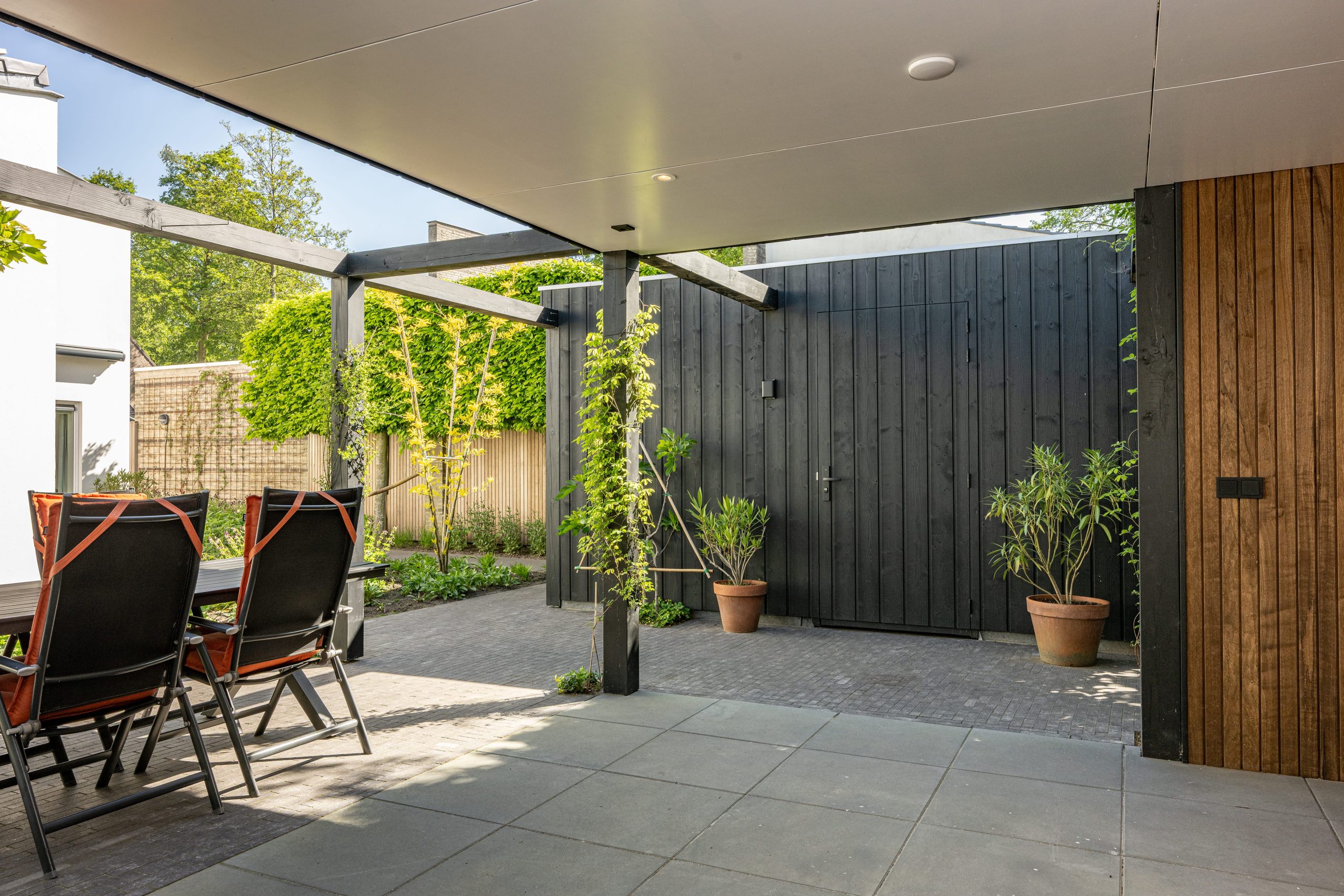 Moderne tuinberging van zwart thermo vuren hout met een overdekt terras van thermo fraké.