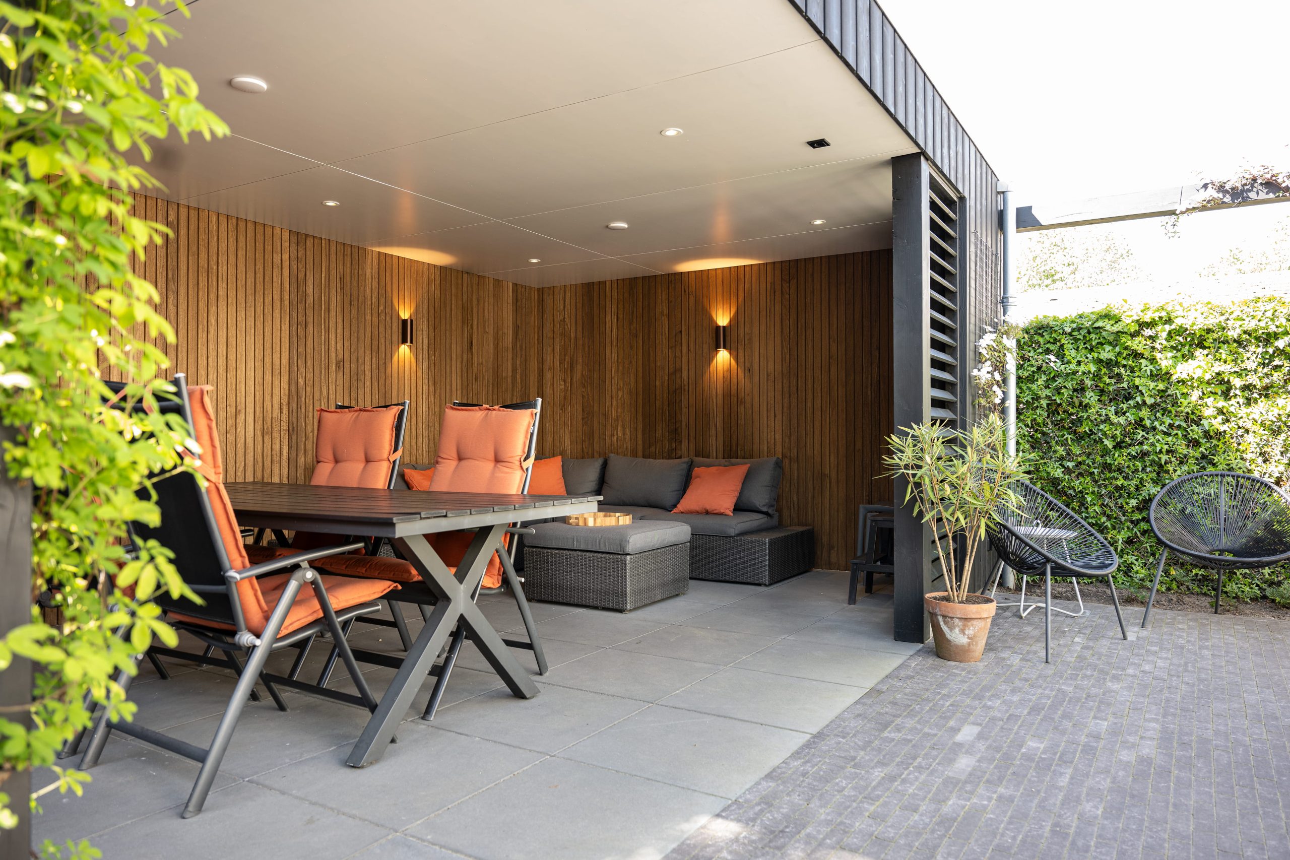 Gezellig overdekt terras met warme thermo fraké houten wanden en een zwarte thermo vuren constructie.