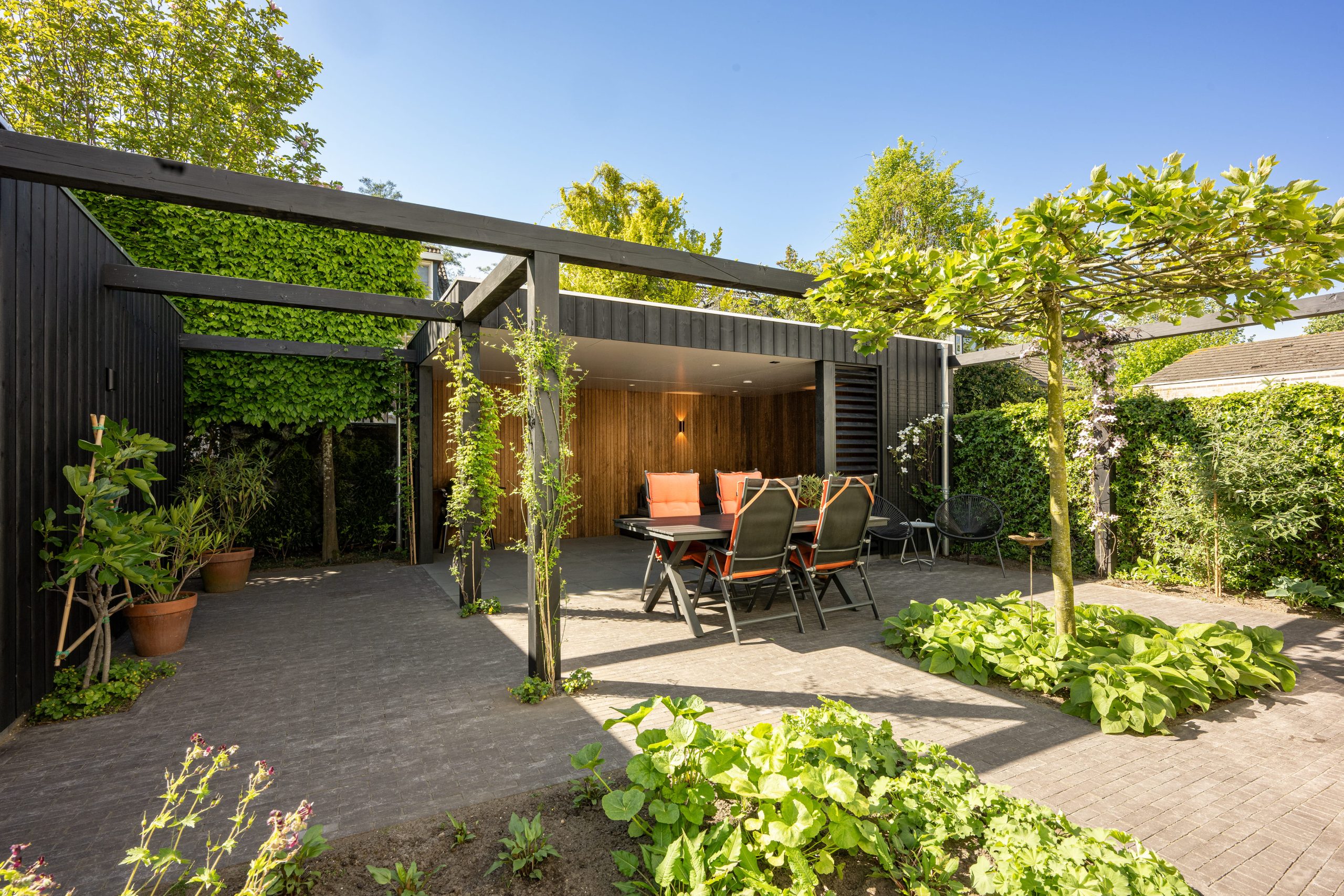 Luxe tuininrichting met een thermo fraké overkapping en een zwarte thermo vuren constructie.