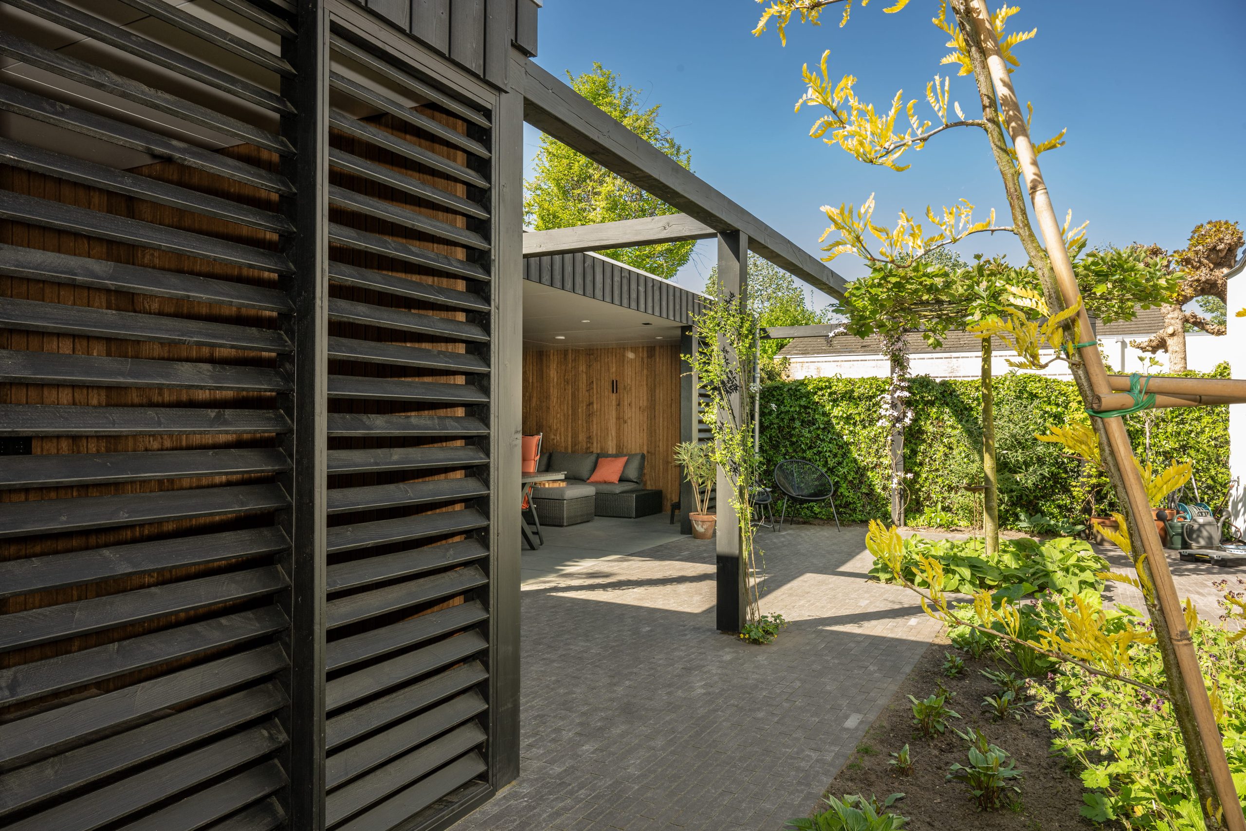 Zicht op een modern overdekt terras met thermo fraké wanden en een zwarte thermo vuren pergola.