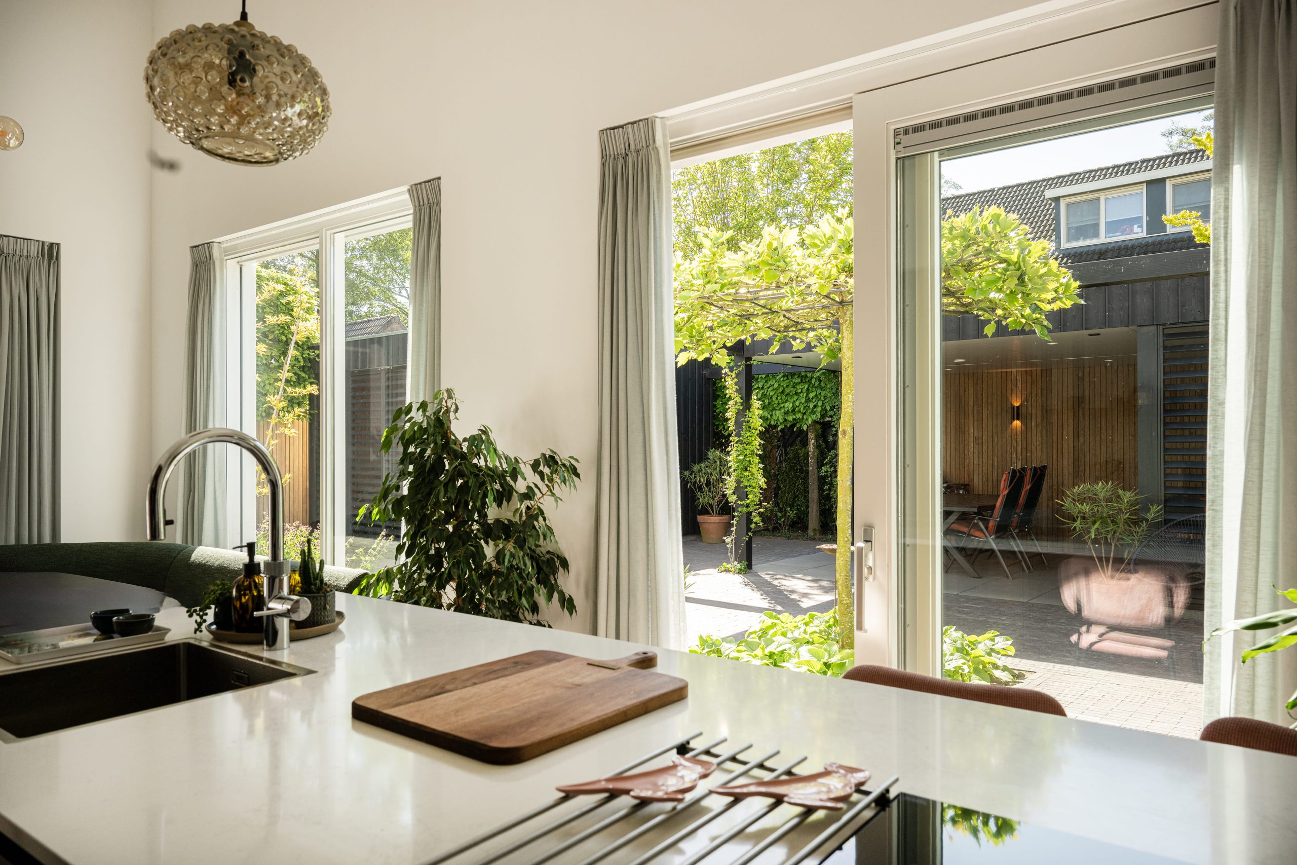 Zicht vanuit de woning op een moderne tuin met overkapping in thermo fraké en zwarte thermo vuren elementen.