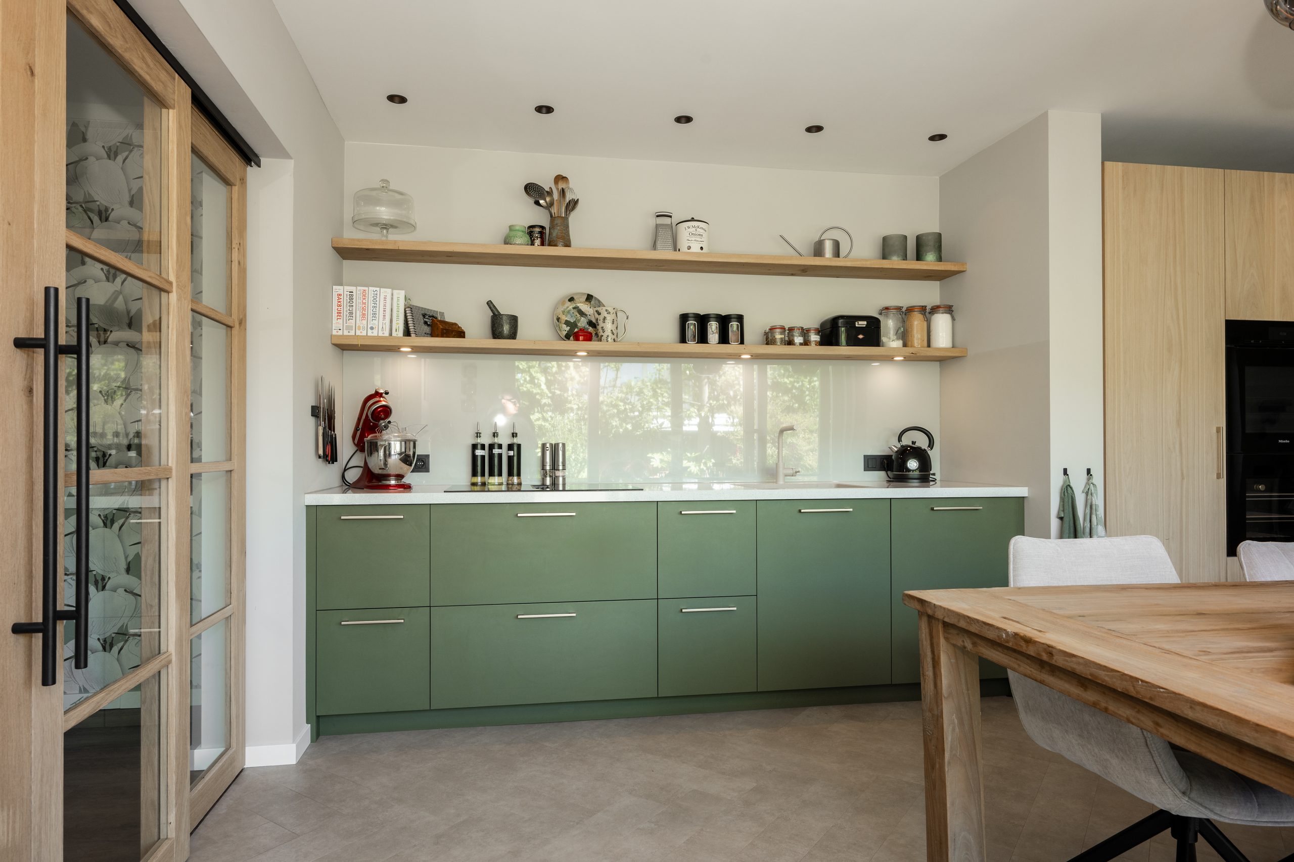 Sfeervolle eethoek met houten tafel en stoelen, direct grenzend aan een moderne keuken met groene fronten.