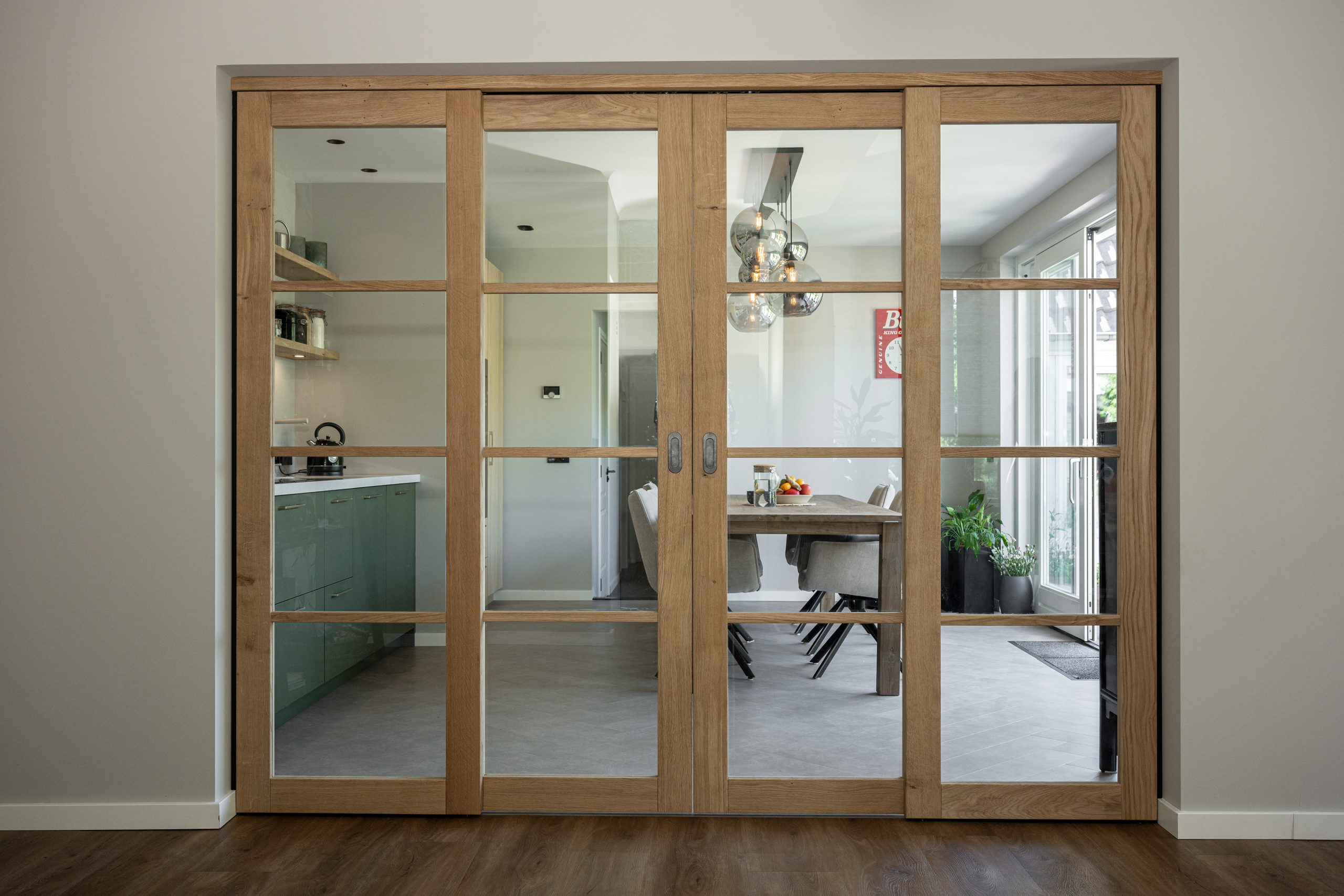 Glazen schuifdeuren met een eikenhouten frame die de doorgang vormen tussen de eetkamer en de keuken.