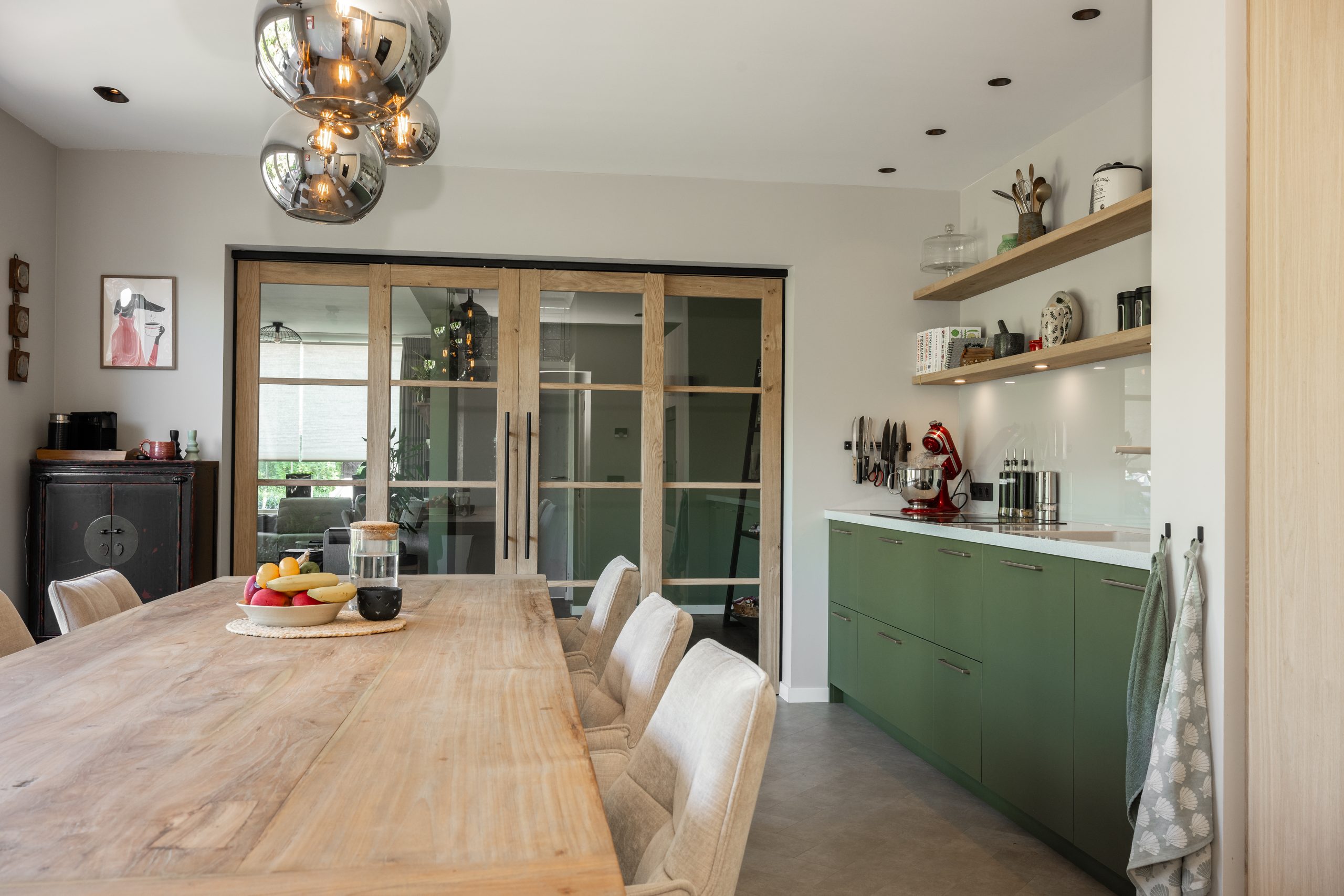 Overzicht van een stijlvol interieur met een moderne groene keuken, houten eettafel en glazen schuifdeuren.