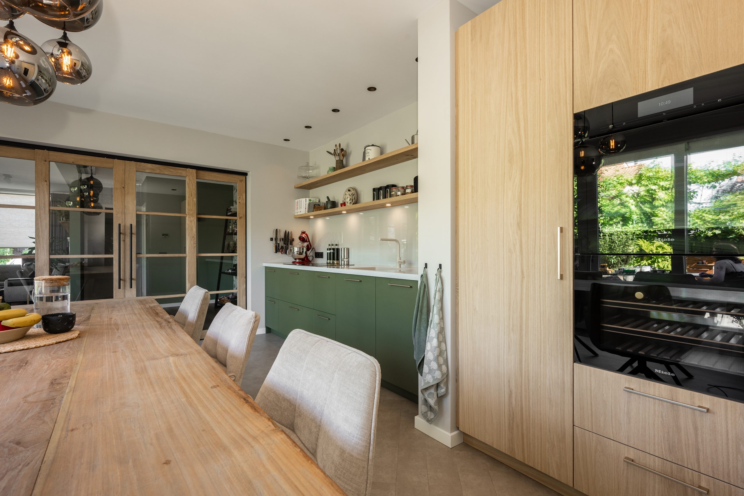 Moderne keukenopstelling naast een glazen schuifdeur met eikenhouten omlijsting en industrieel interieur.