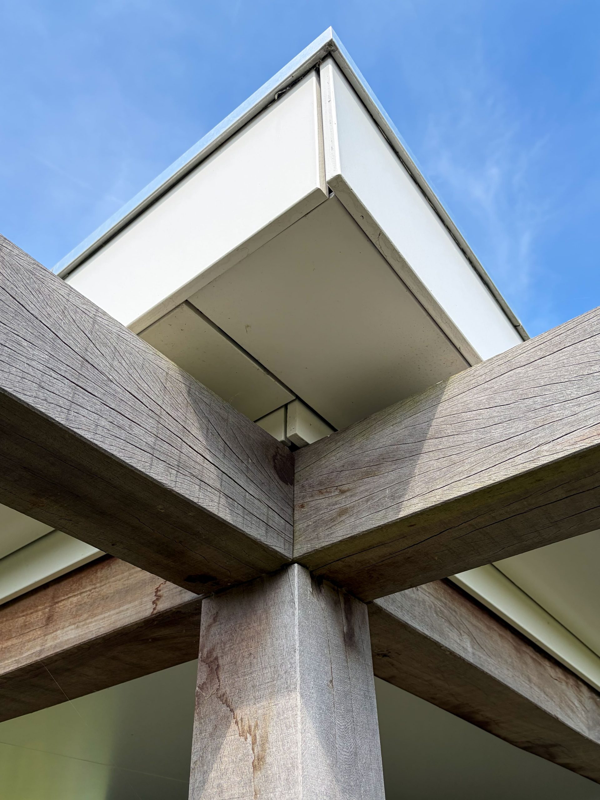 Architectonisch detail van de robuuste houten balkenconstructie en strakke dakrand van een moderne overkapping.