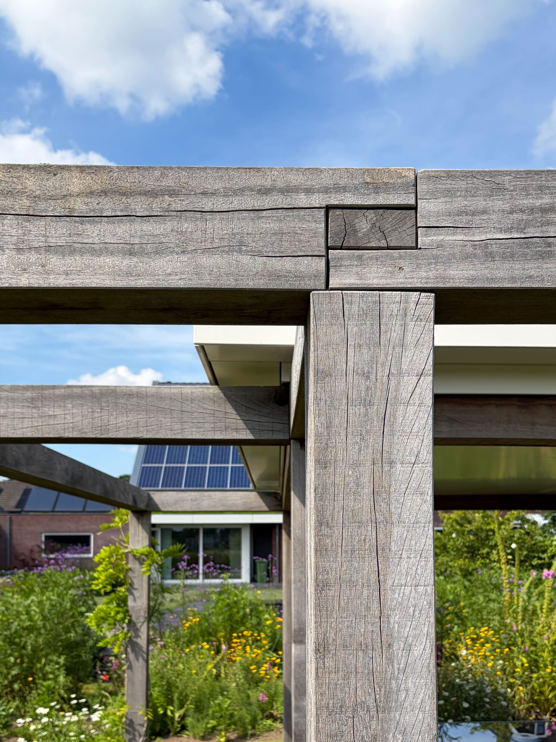 Close-up van de robuuste houten verbindingen en balken van een pergola tegen een heldere blauwe lucht.