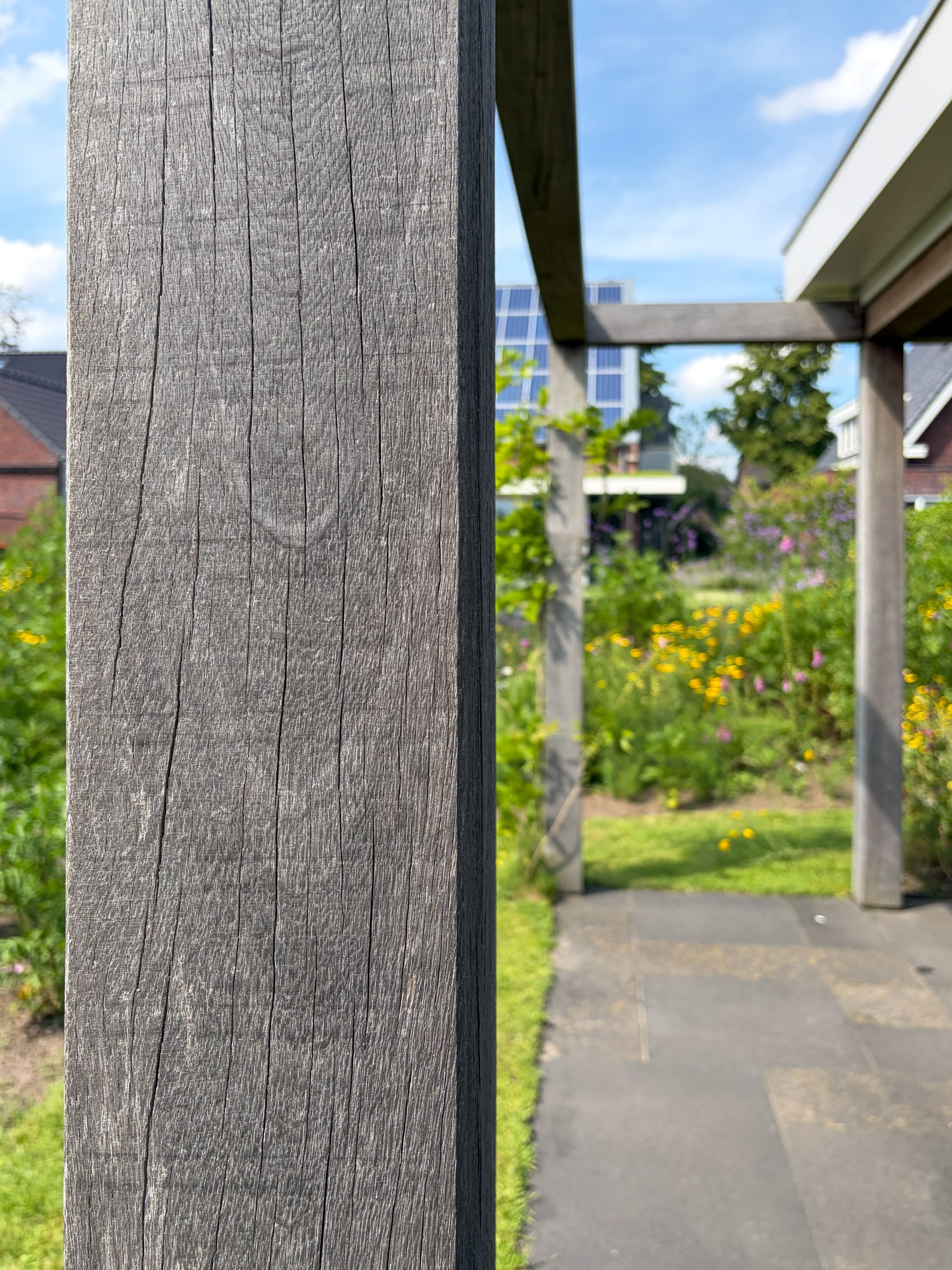 Detail van de verweerde houtnerf van een houten pergola-paal met een vage achtergrond van een bloemrijke tuin.